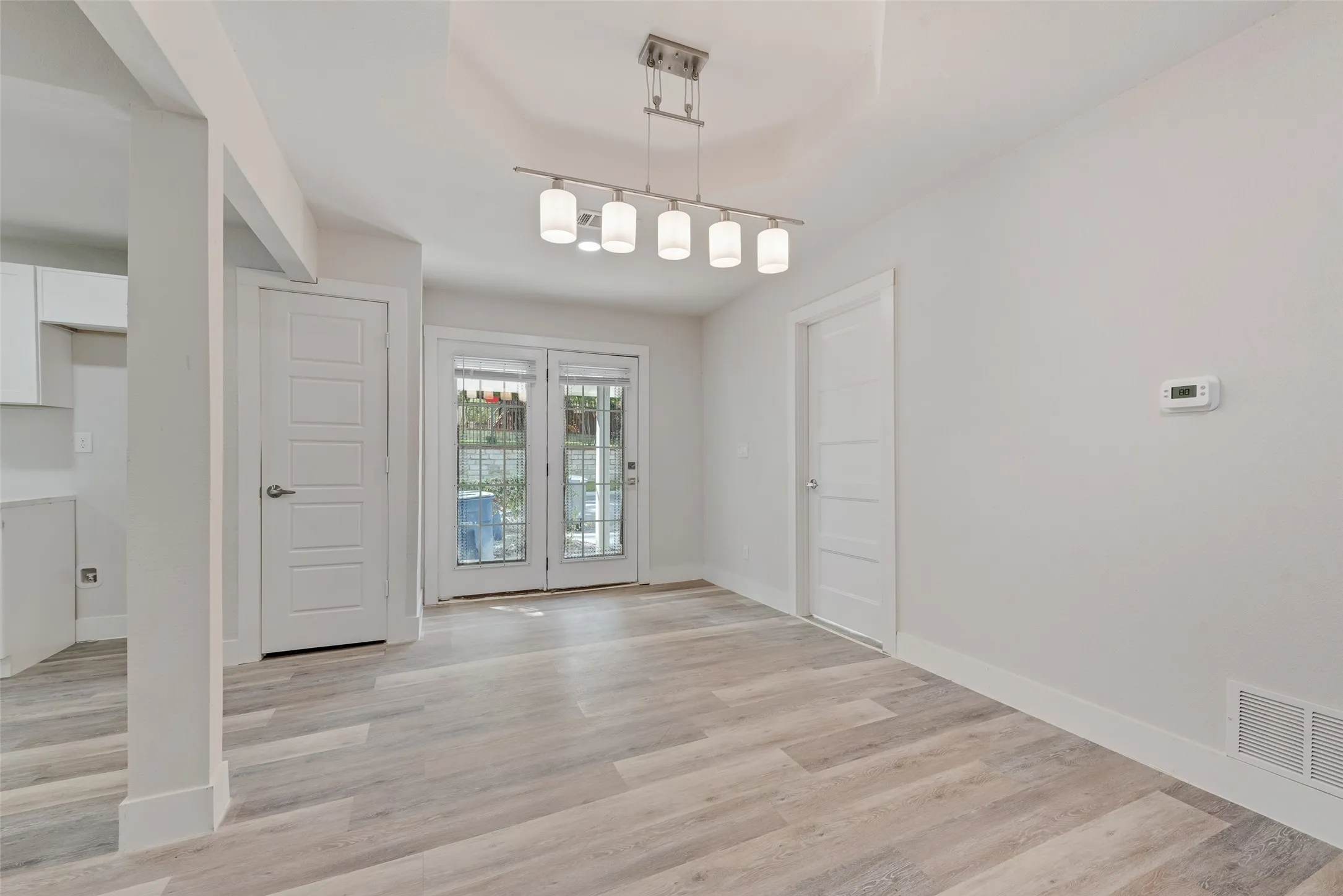Light wood-finish flooring, white walls, and a contemporary linear chandelier with frosted glass shades