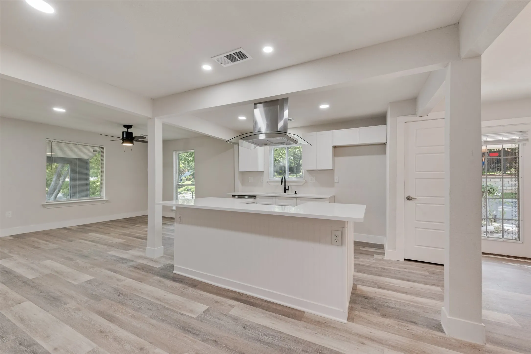 Open-concept living space featuring wood-finish flooring, recessed lighting, and a contemporary kitchen island with a built-in range hood