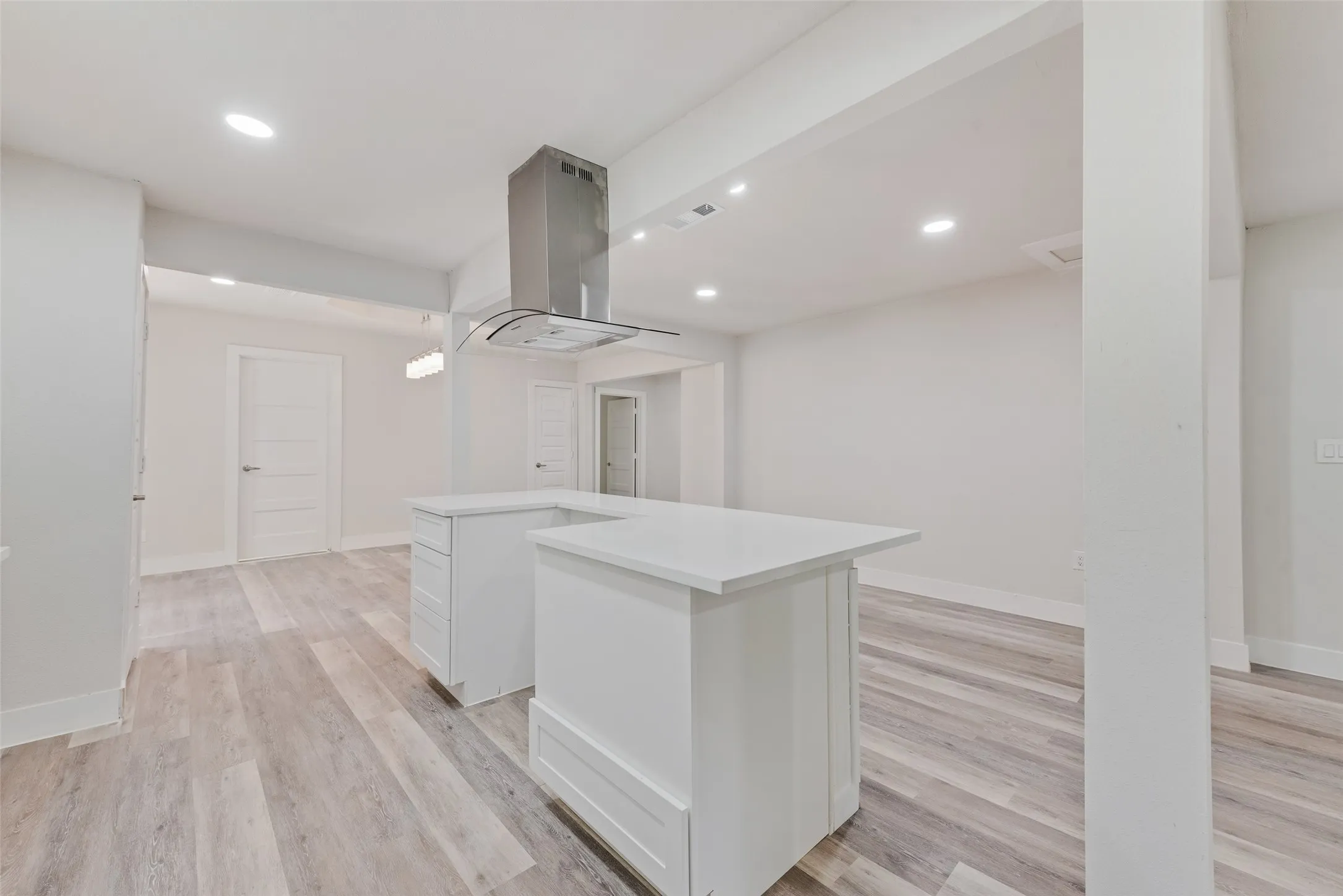 White kitchen island with a light-toned countertop, stainless steel range hood, wood-finish flooring, and recessed ceiling lighting