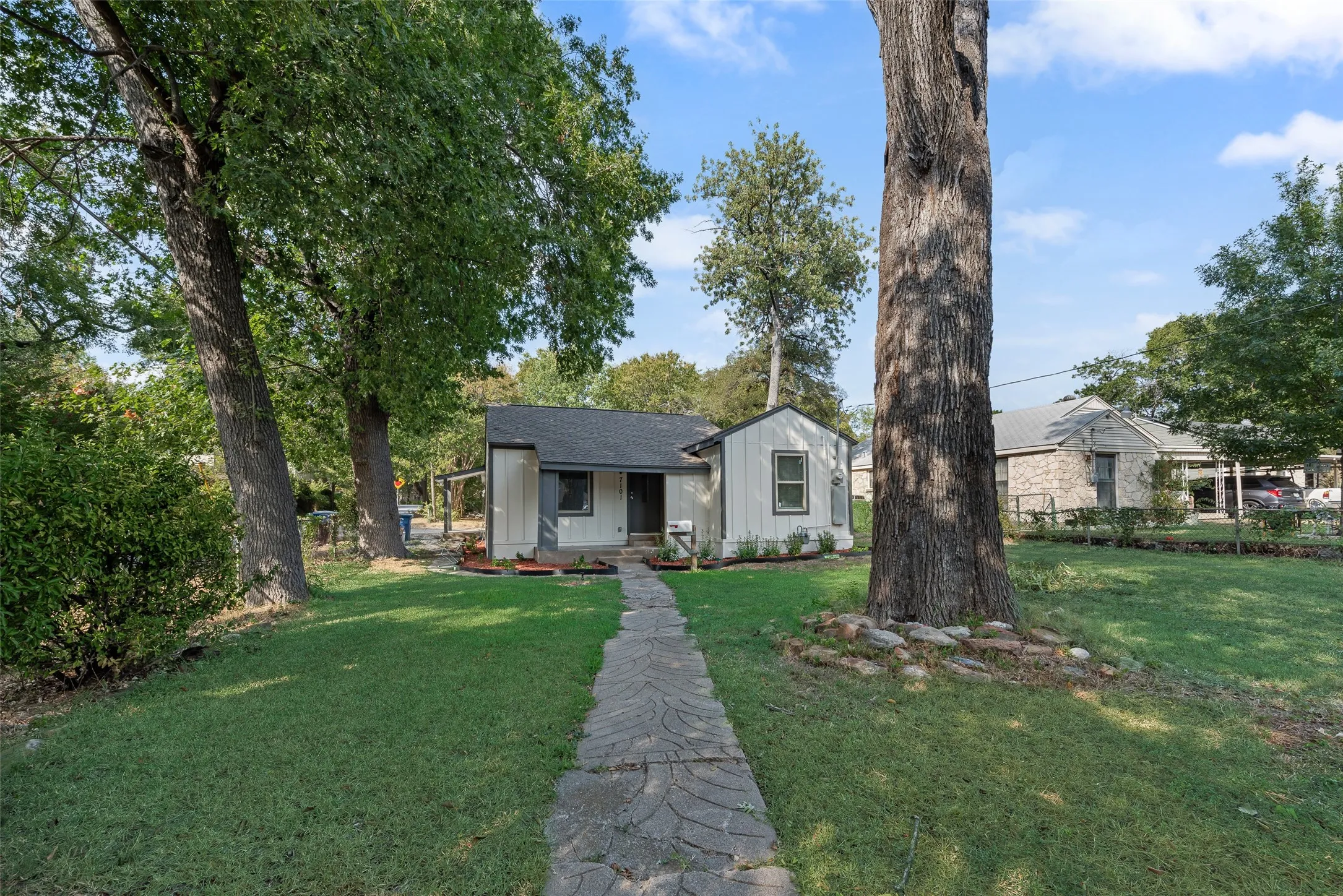 White siding exterior with a dark trim, featuring a dark roof and a stone walkway