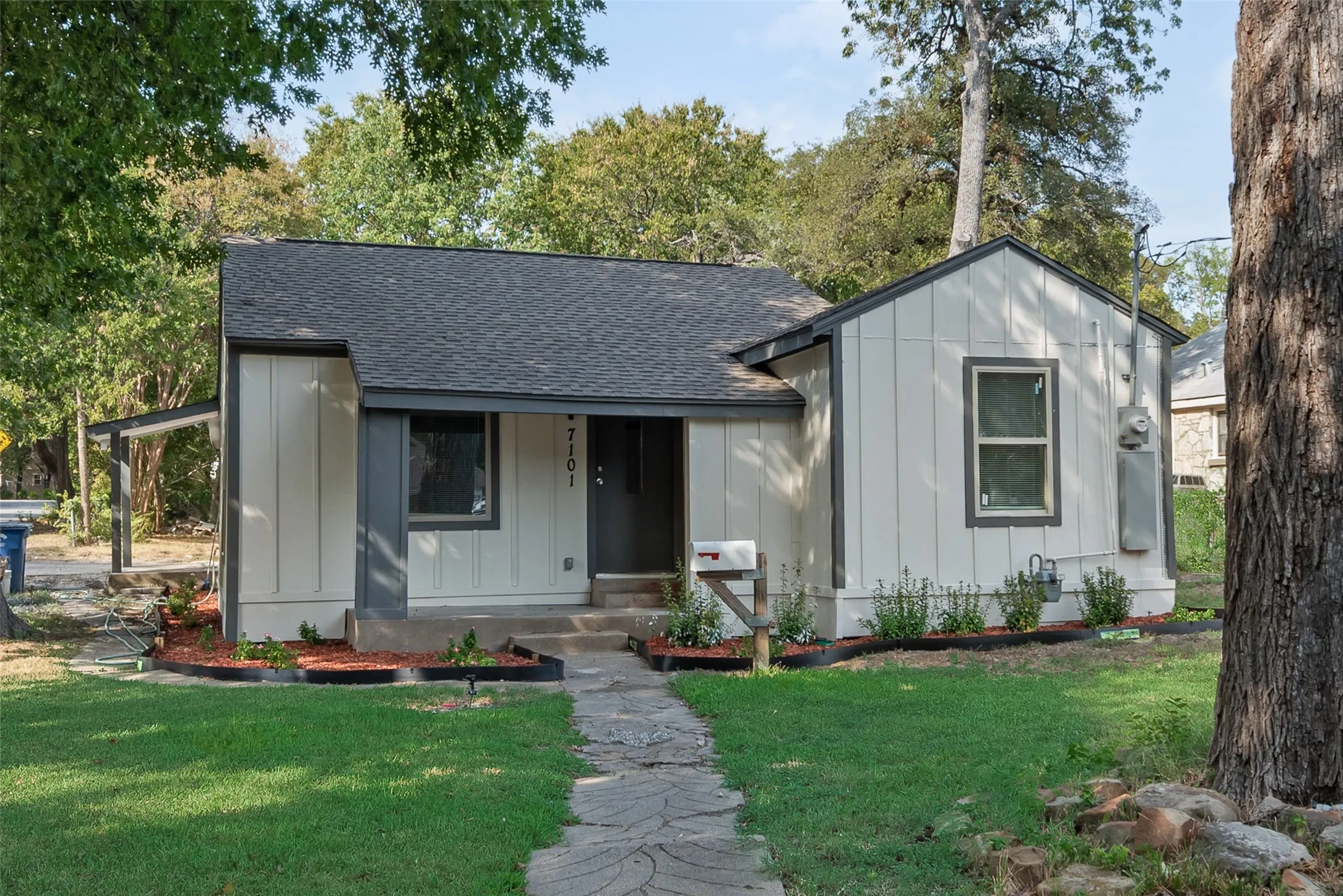 Exterior featuring light-colored siding with dark trim, a dark shingle roof, and a stone-paver walkway