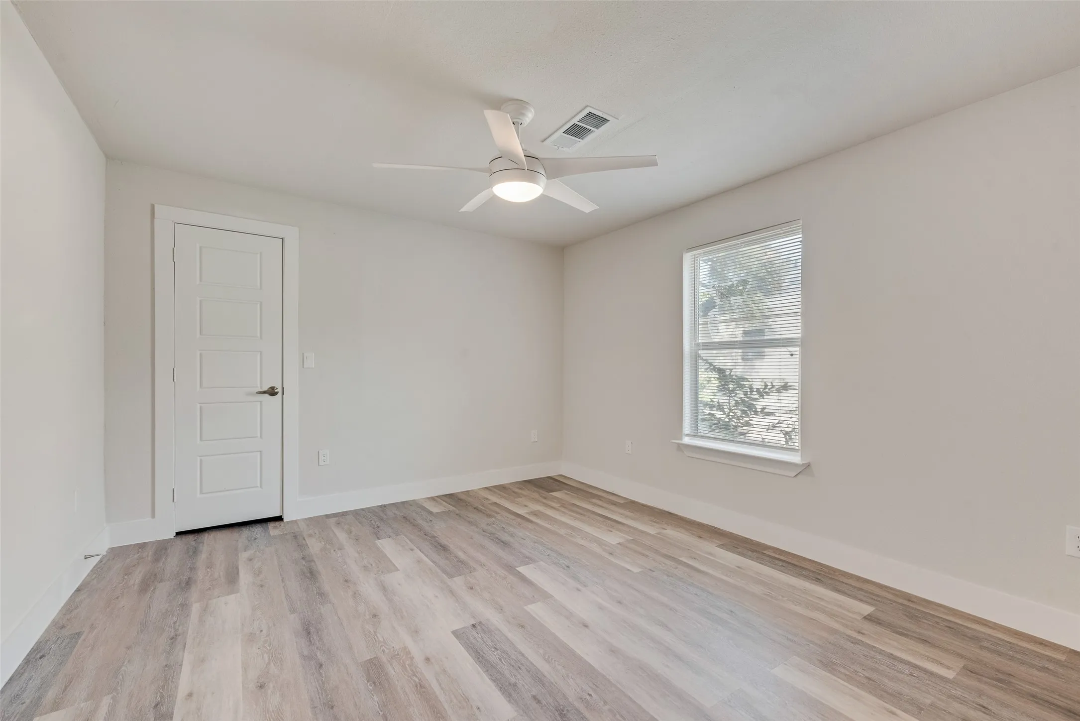 Wood-finish flooring, white paneled door, ceiling fan with integrated lighting, and a single window