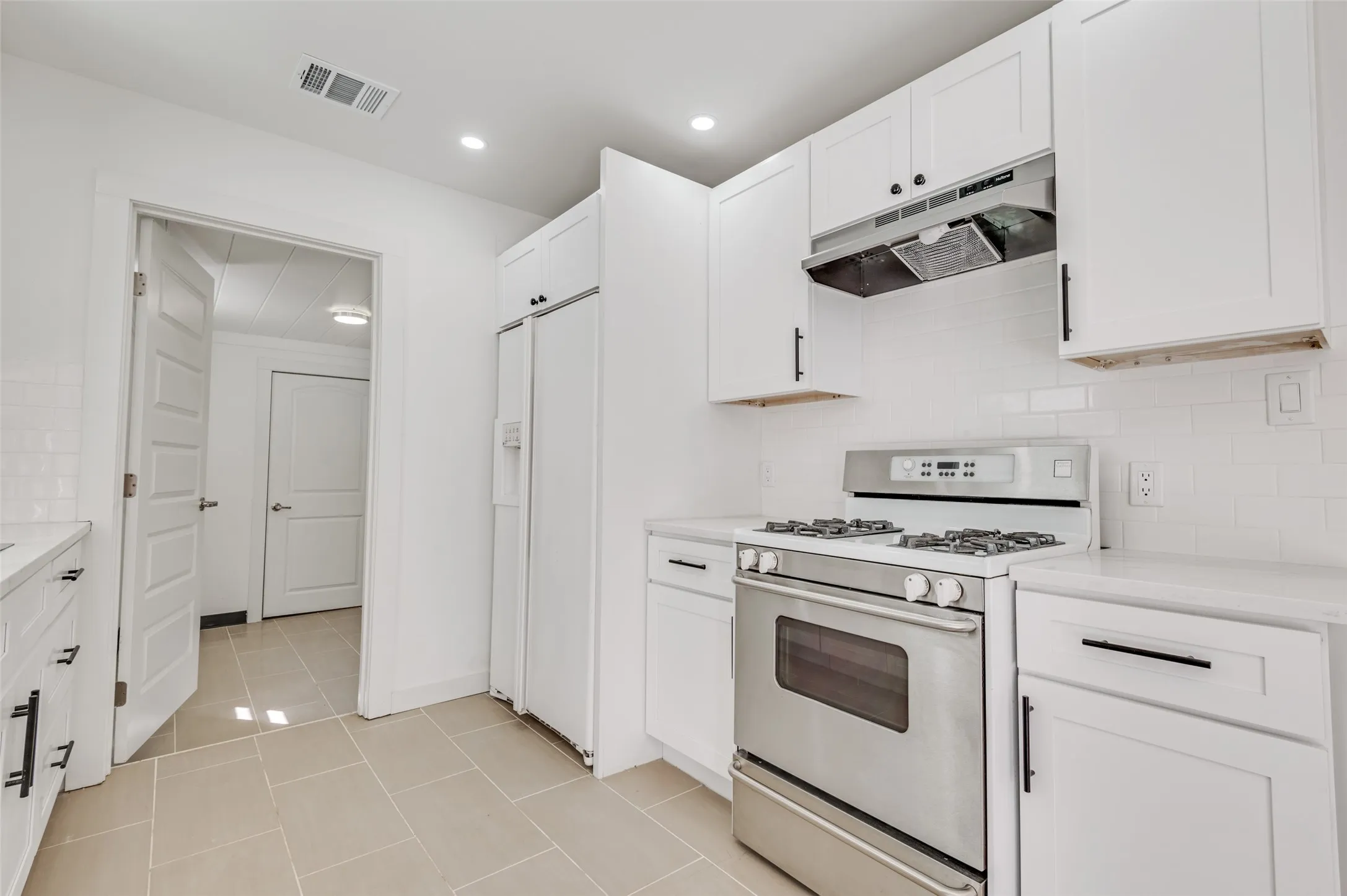 White kitchen cabinetry with black hardware, stainless steel gas range, subway tile backsplash, and light-toned floor tiling