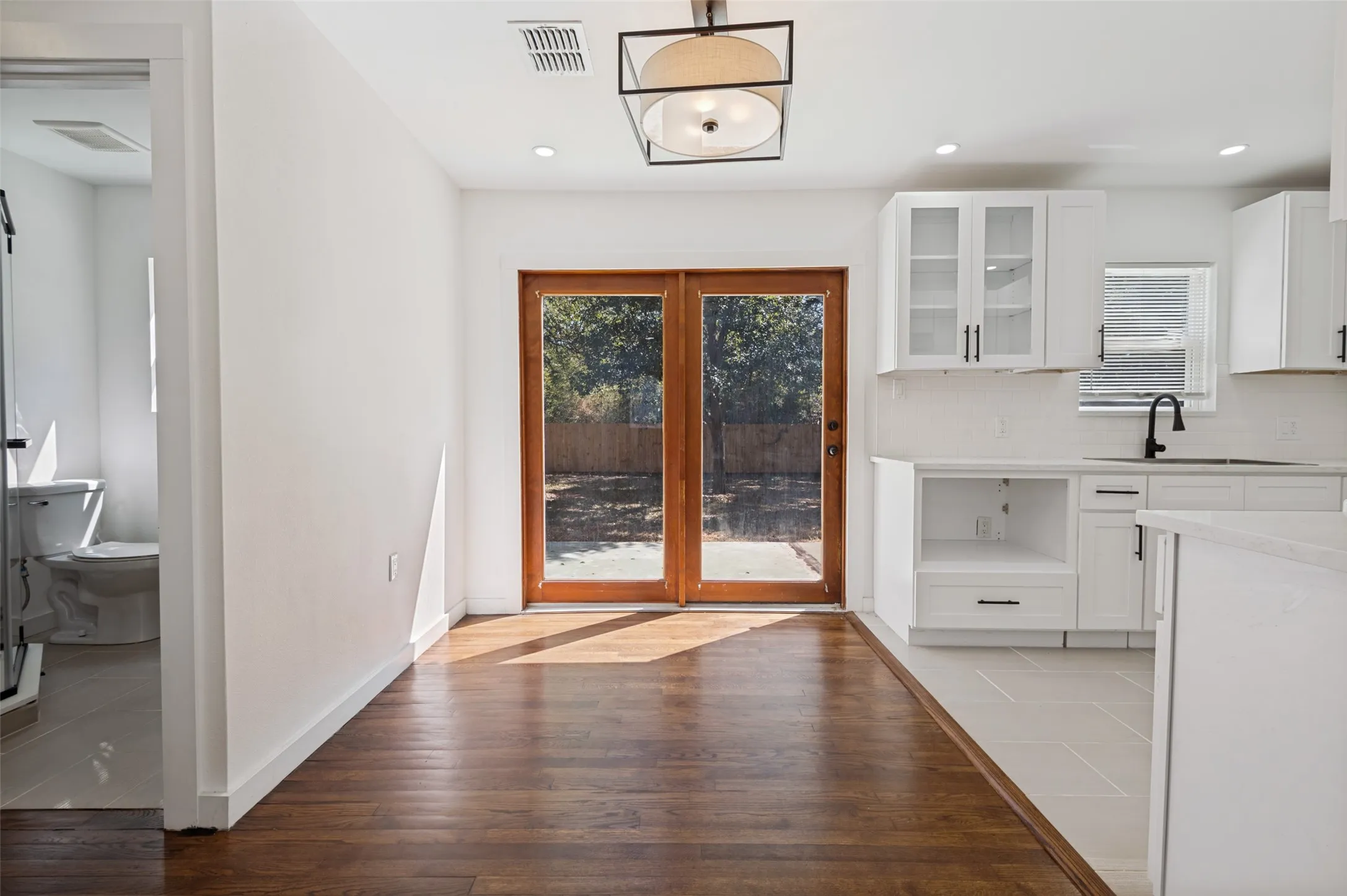 Wood-finish flooring, white cabinetry with glass-front uppers, French doors, recessed lighting, and a contemporary ceiling fixture