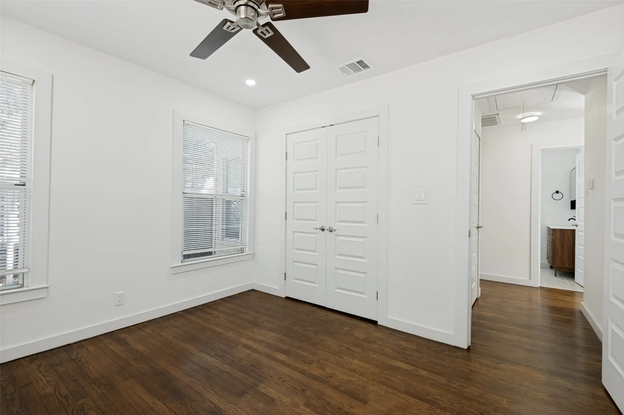 Wood-finish flooring, white walls, two windows with blinds, recessed lighting, and a ceiling fan