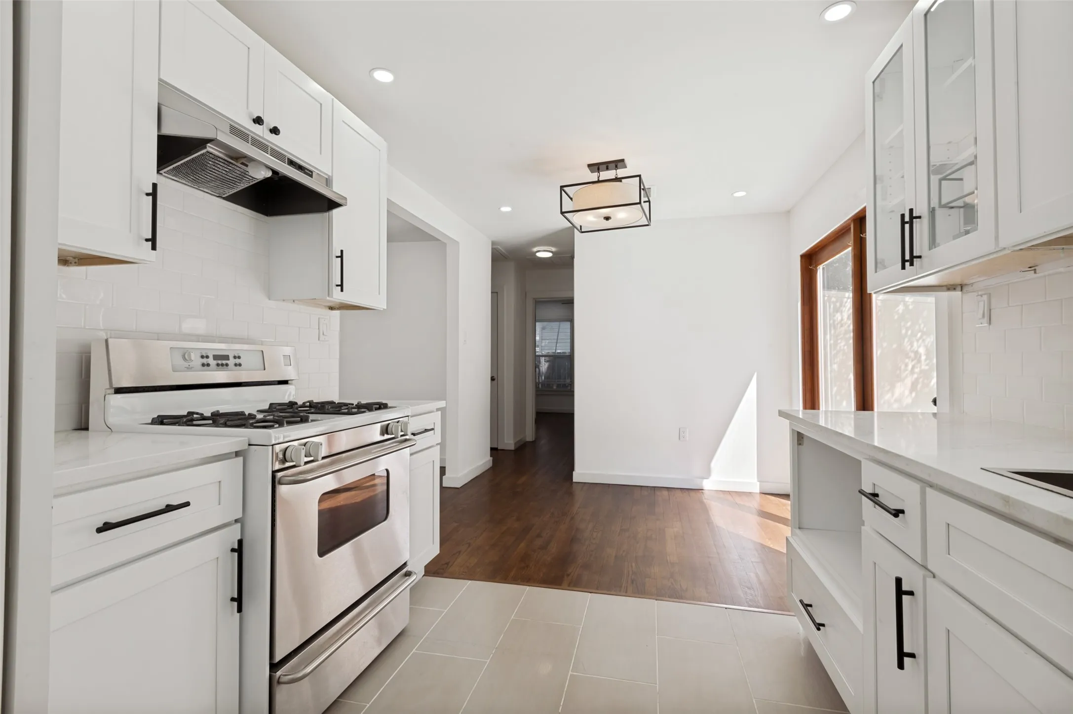White cabinetry with black hardware, stainless steel range, white subway tile backsplash, white countertops, recessed lighting, and wood-finish flooring