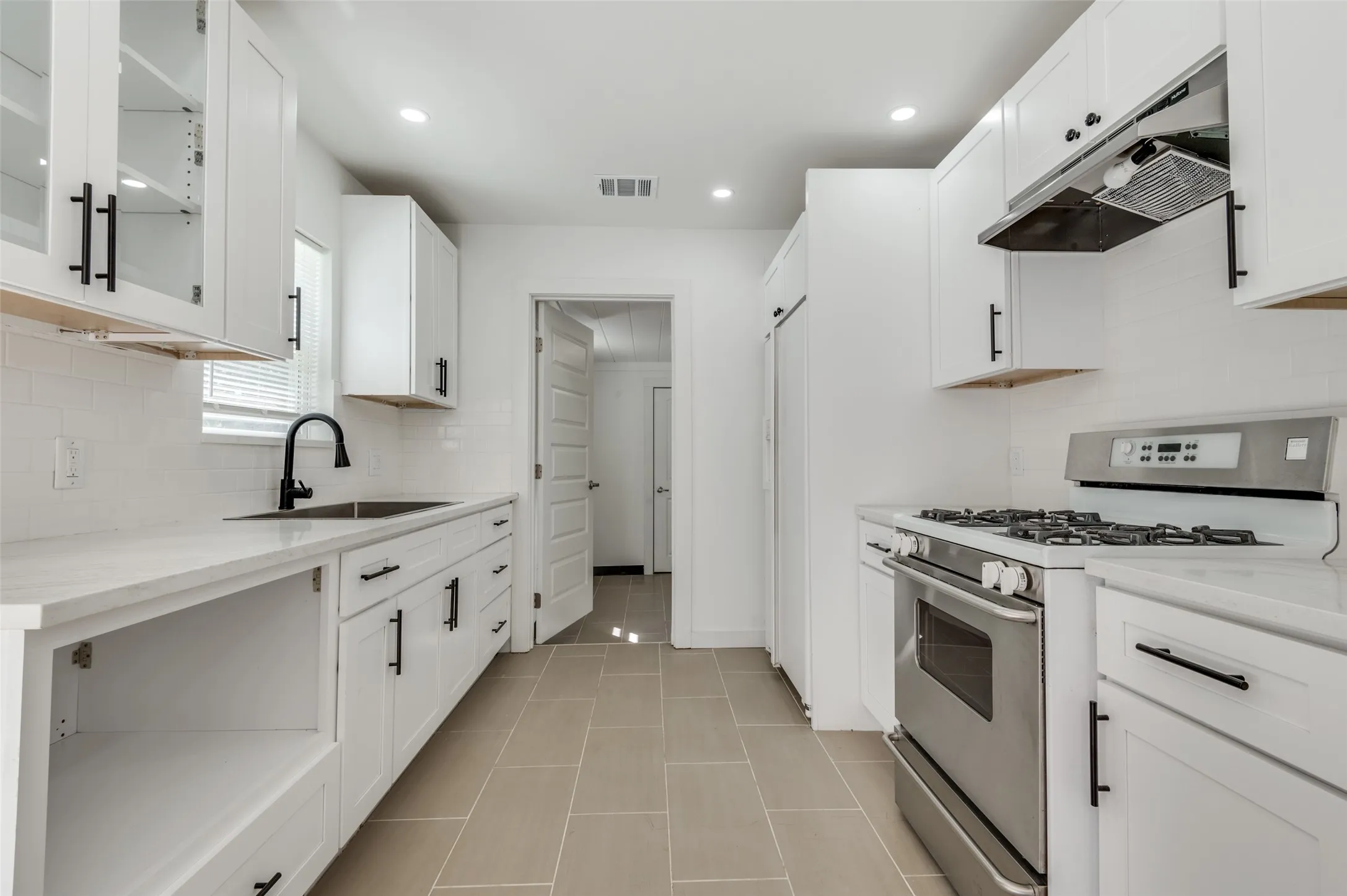 Kitchen featuring white shaker cabinetry, stainless steel appliances, light-toned countertops, tile backsplash, and tile flooring