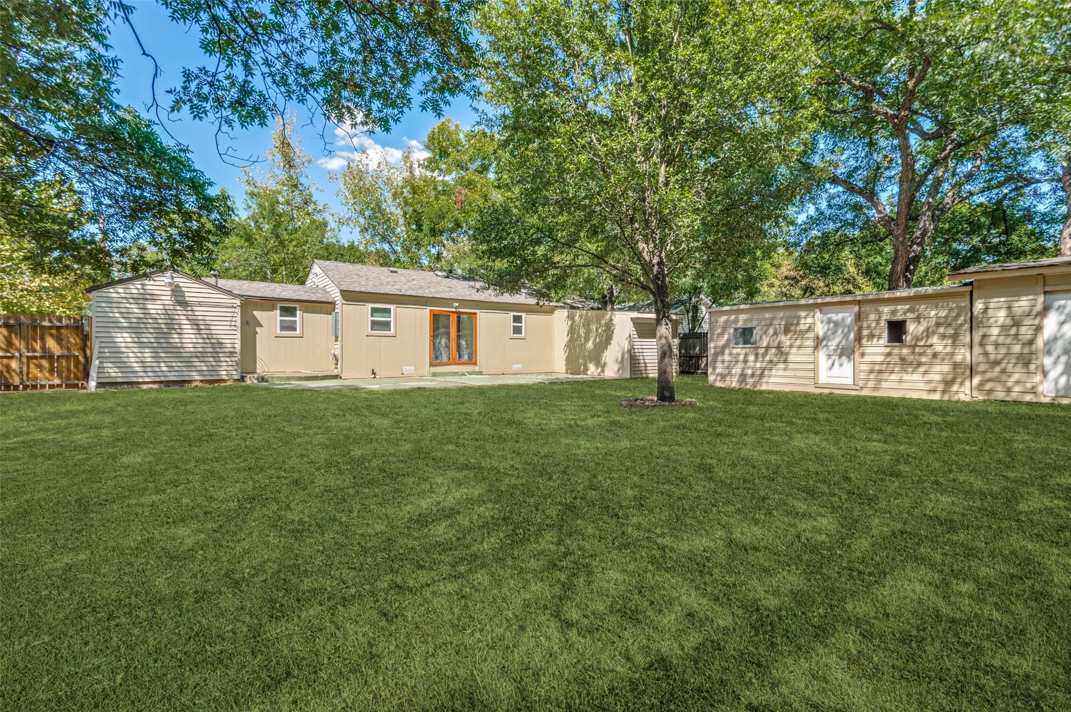 Expansive grassy yard with mature trees, a concrete patio, and a wood privacy fence