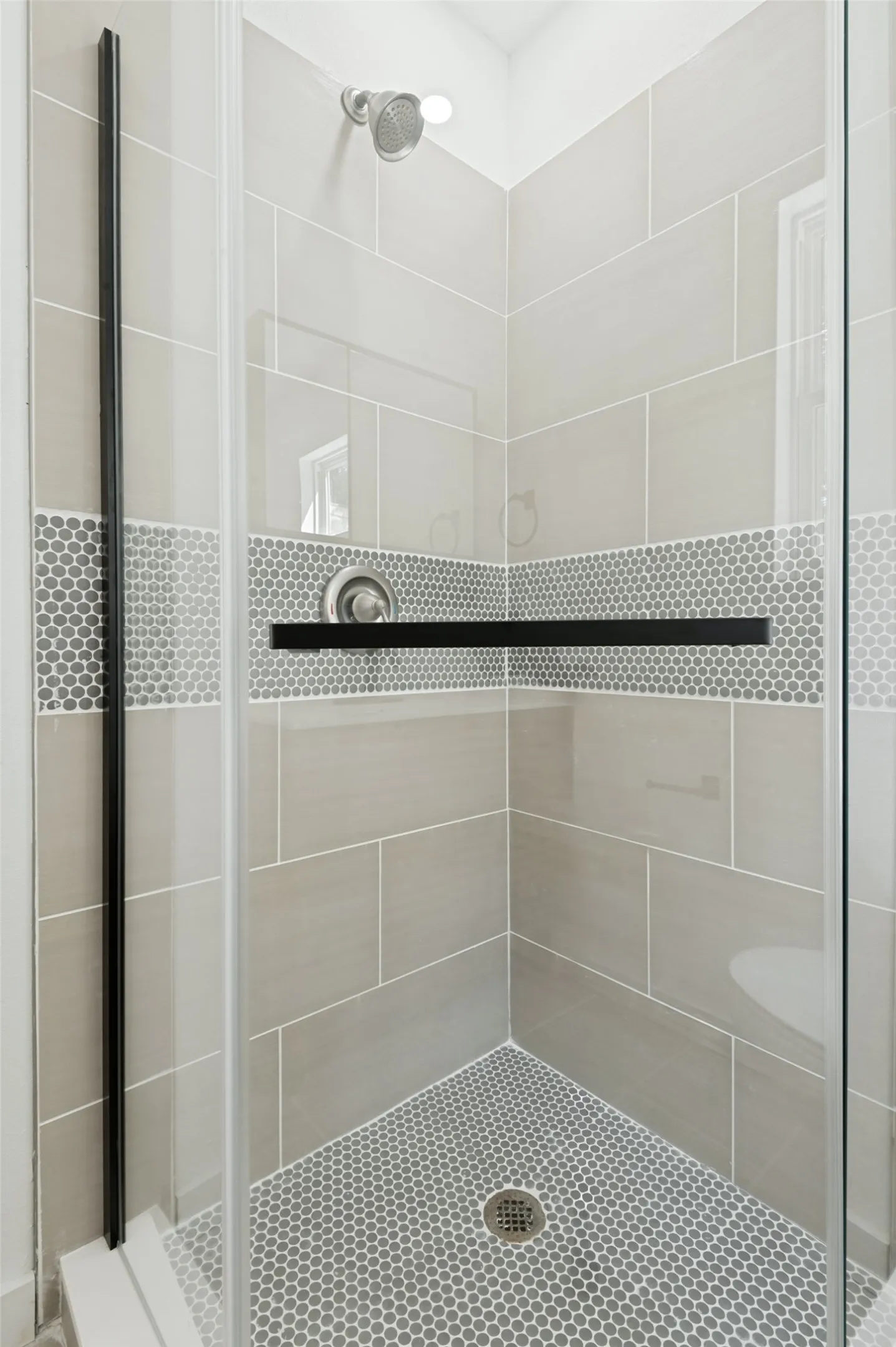 Glass-enclosed shower featuring large format wall tiles, a hexagonal mosaic floor, a mosaic accent band, and a built-in shelf