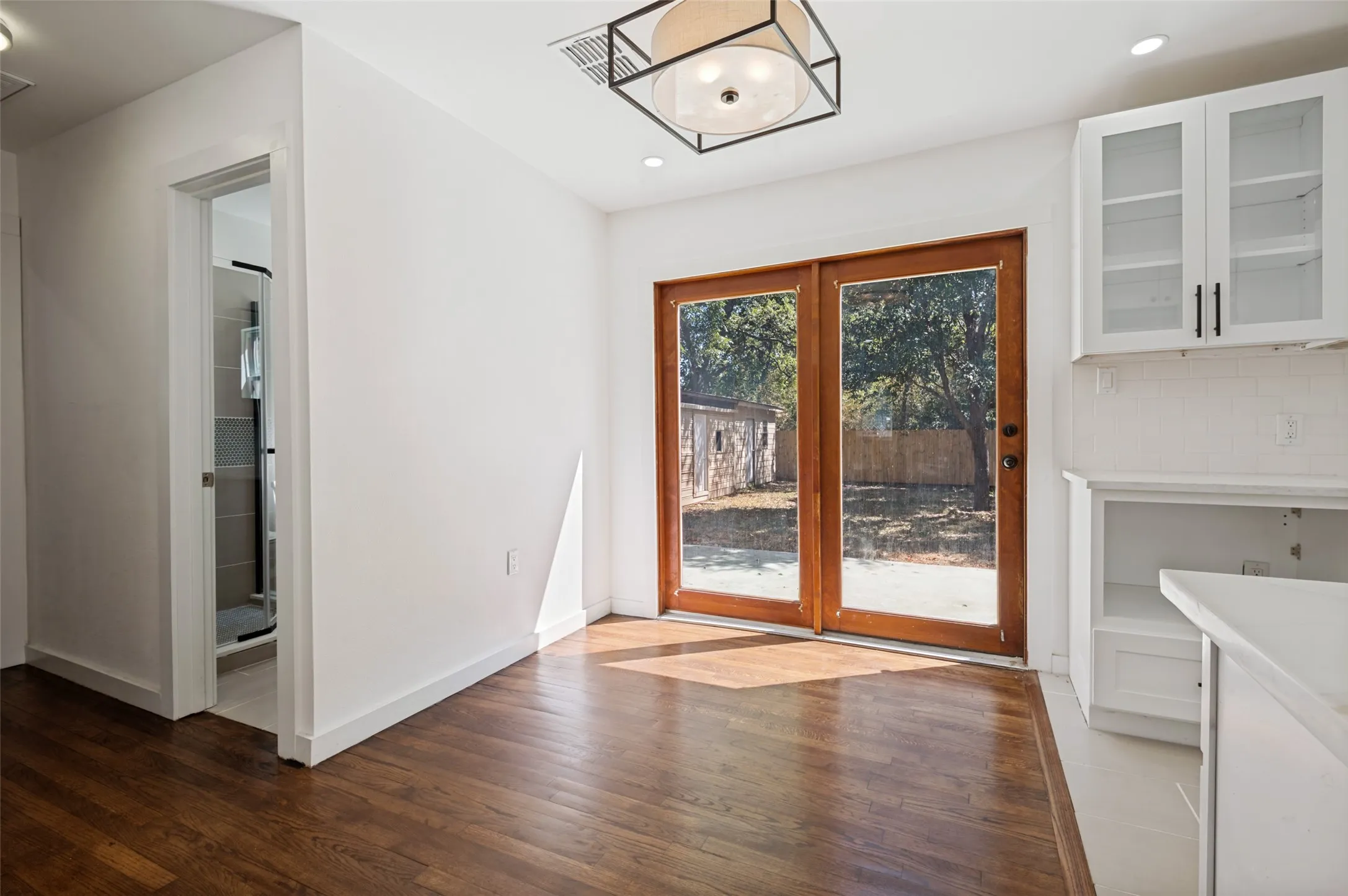 Wood-finish flooring, white cabinetry with glass inserts, transom ceiling light fixture, and double glass-paneled doors