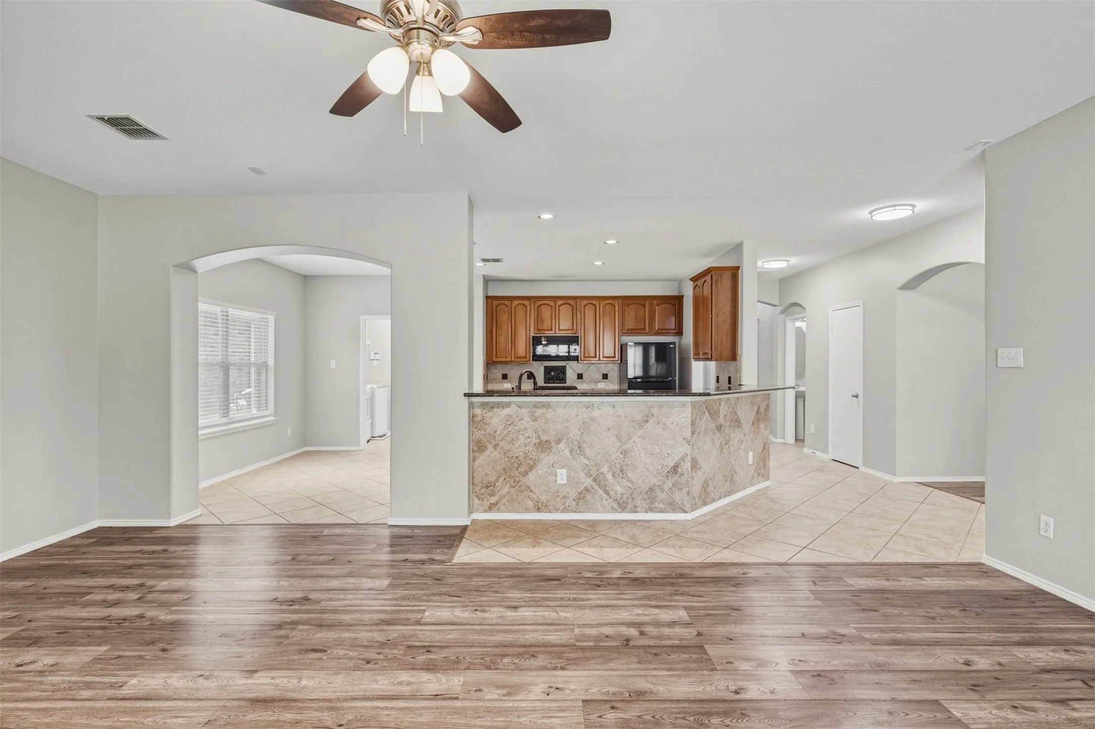 Open-concept living space with wood-finish flooring, a ceiling fan, and arched doorways