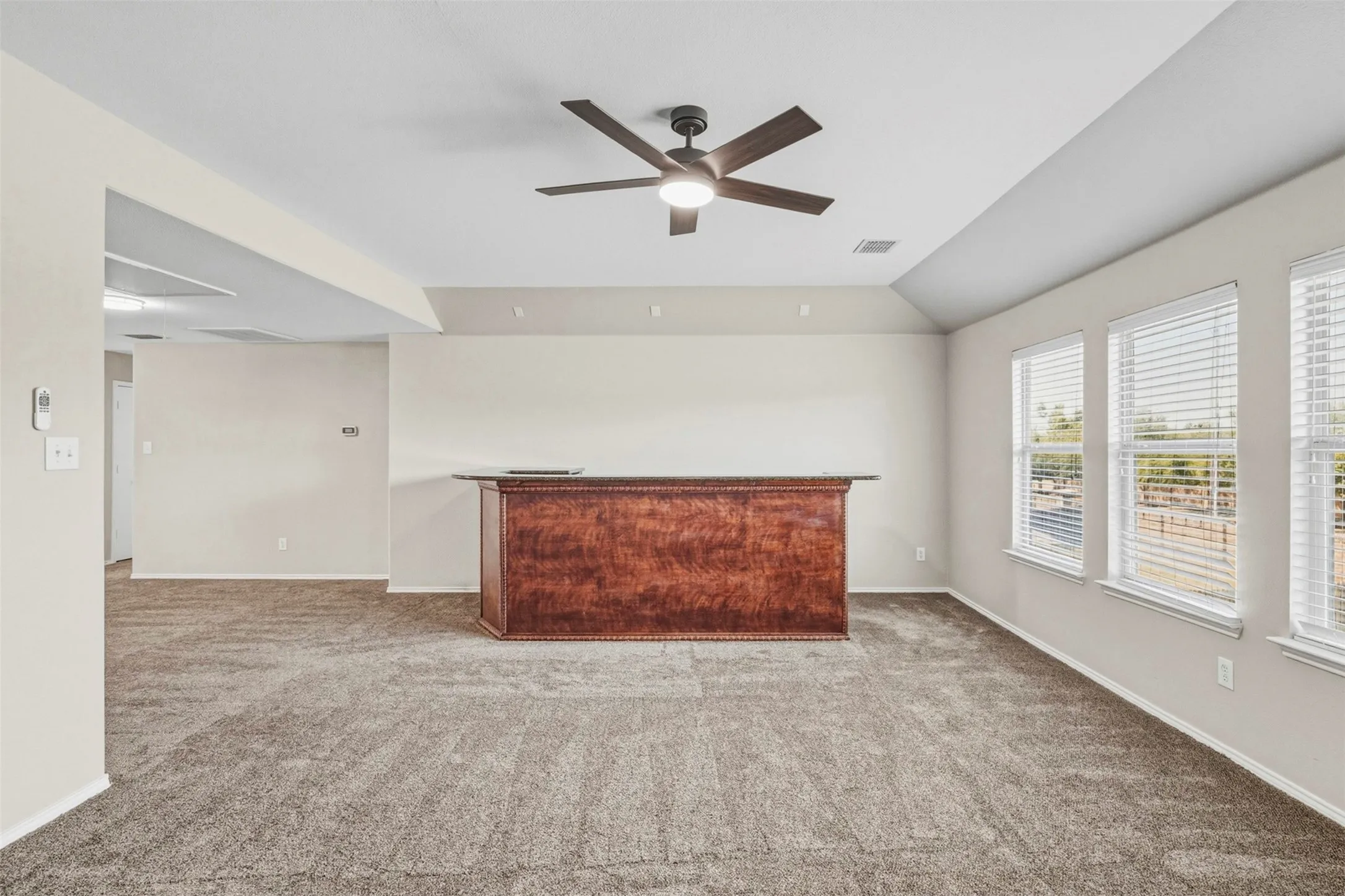 Recessed ceiling with a dark-tone ceiling fan, light-toned walls, and a built-in wooden bar