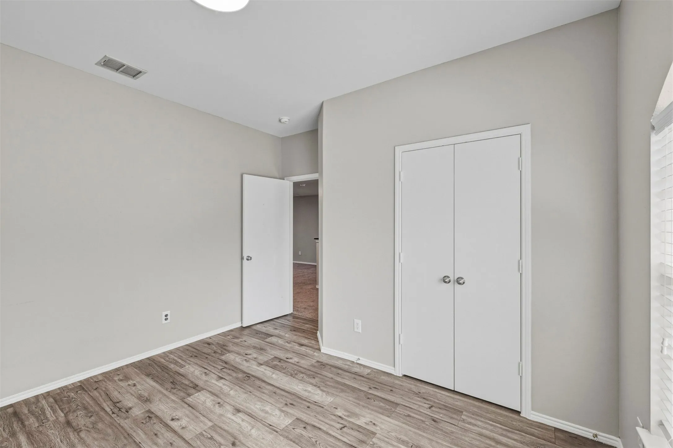 Wood-finish flooring, light grey wall paint, bi-fold closet doors, white trim, and a flush mount ceiling light