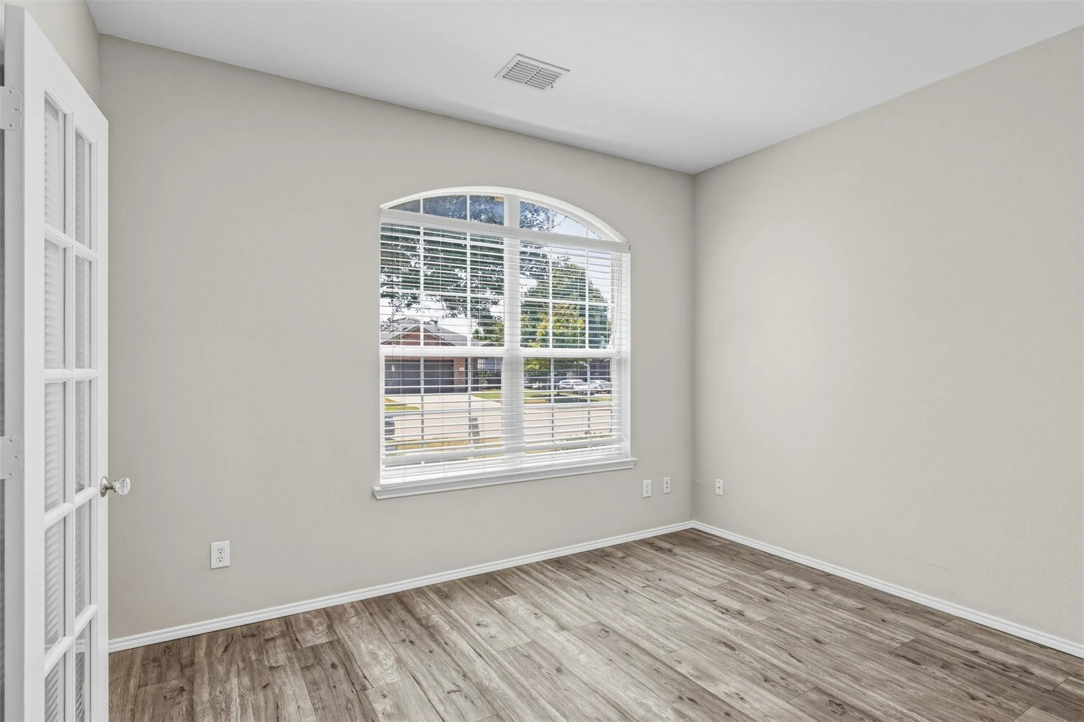 Arch-top window with blinds, wood-finish flooring, white trim throughout, and a French door entry