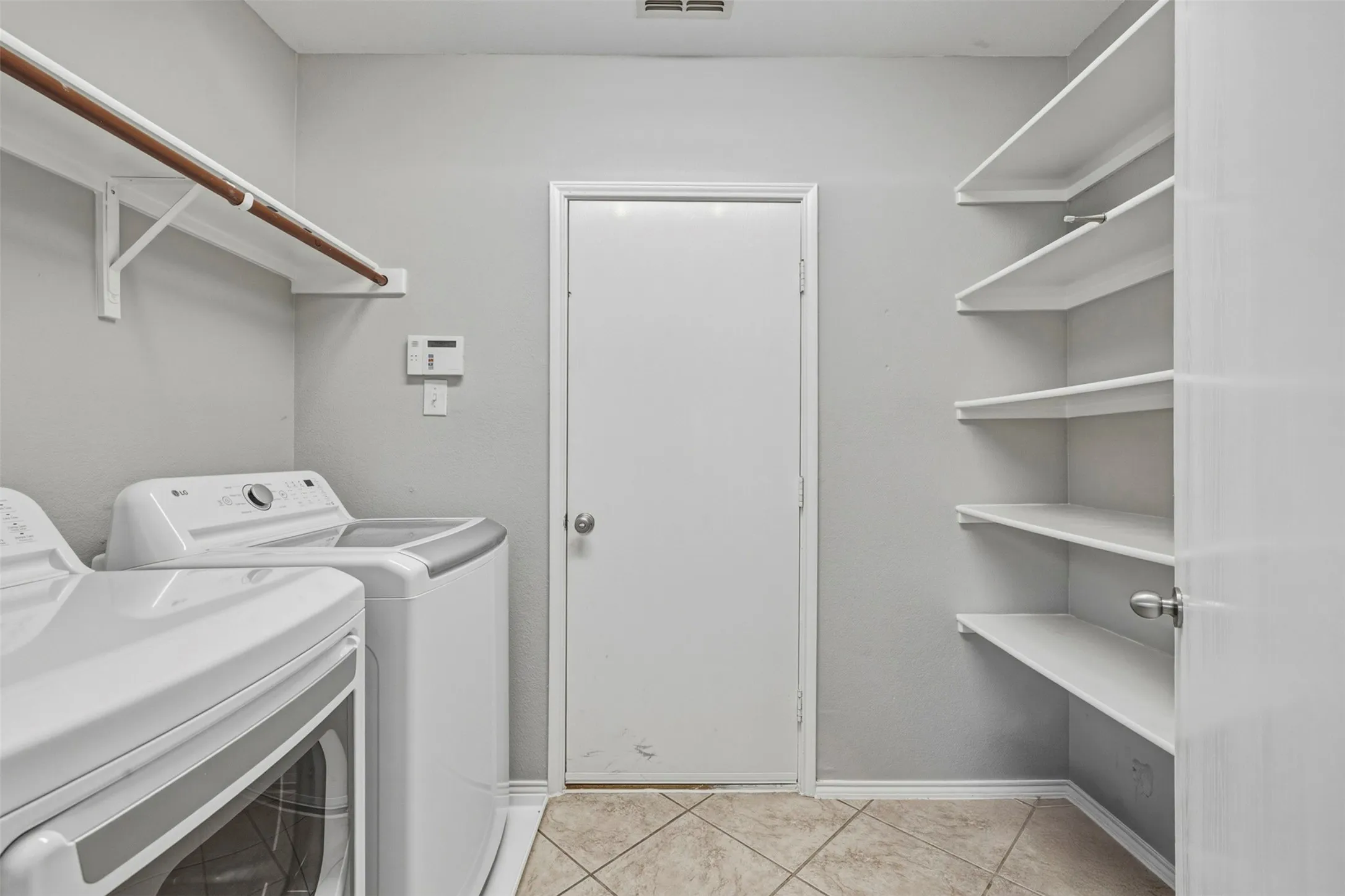 Laundry room featuring tile flooring, built-in shelving, and a mounted clothing rod