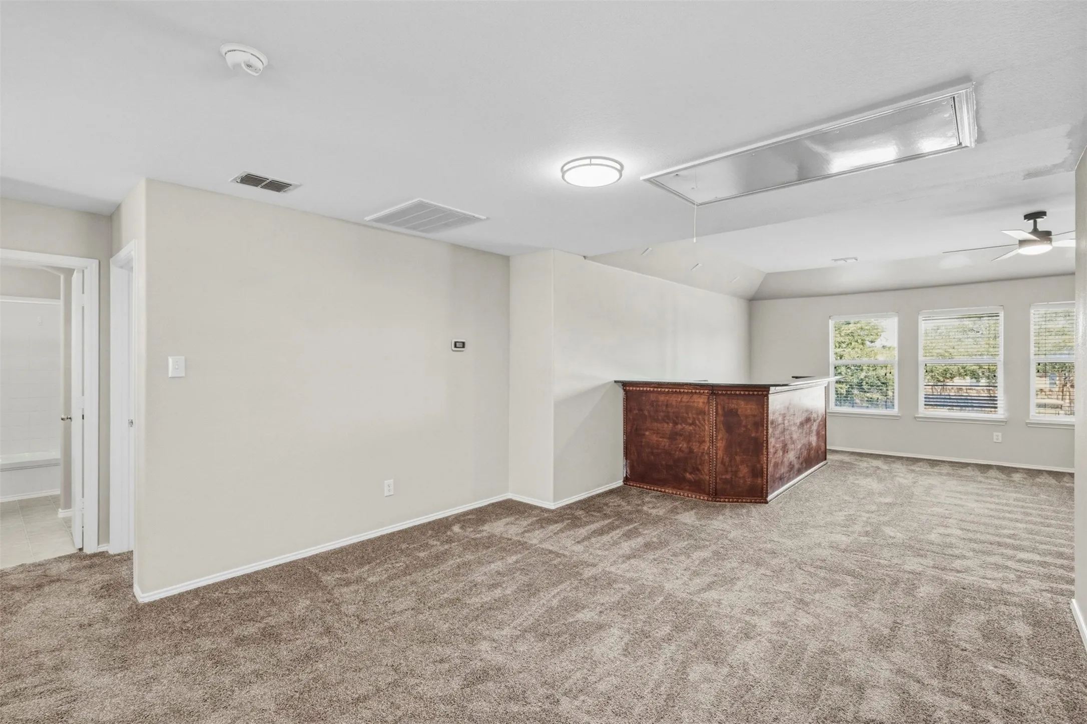 Expansive carpeted area featuring multiple windows, a built-in wood-finish bar, and a ceiling fan