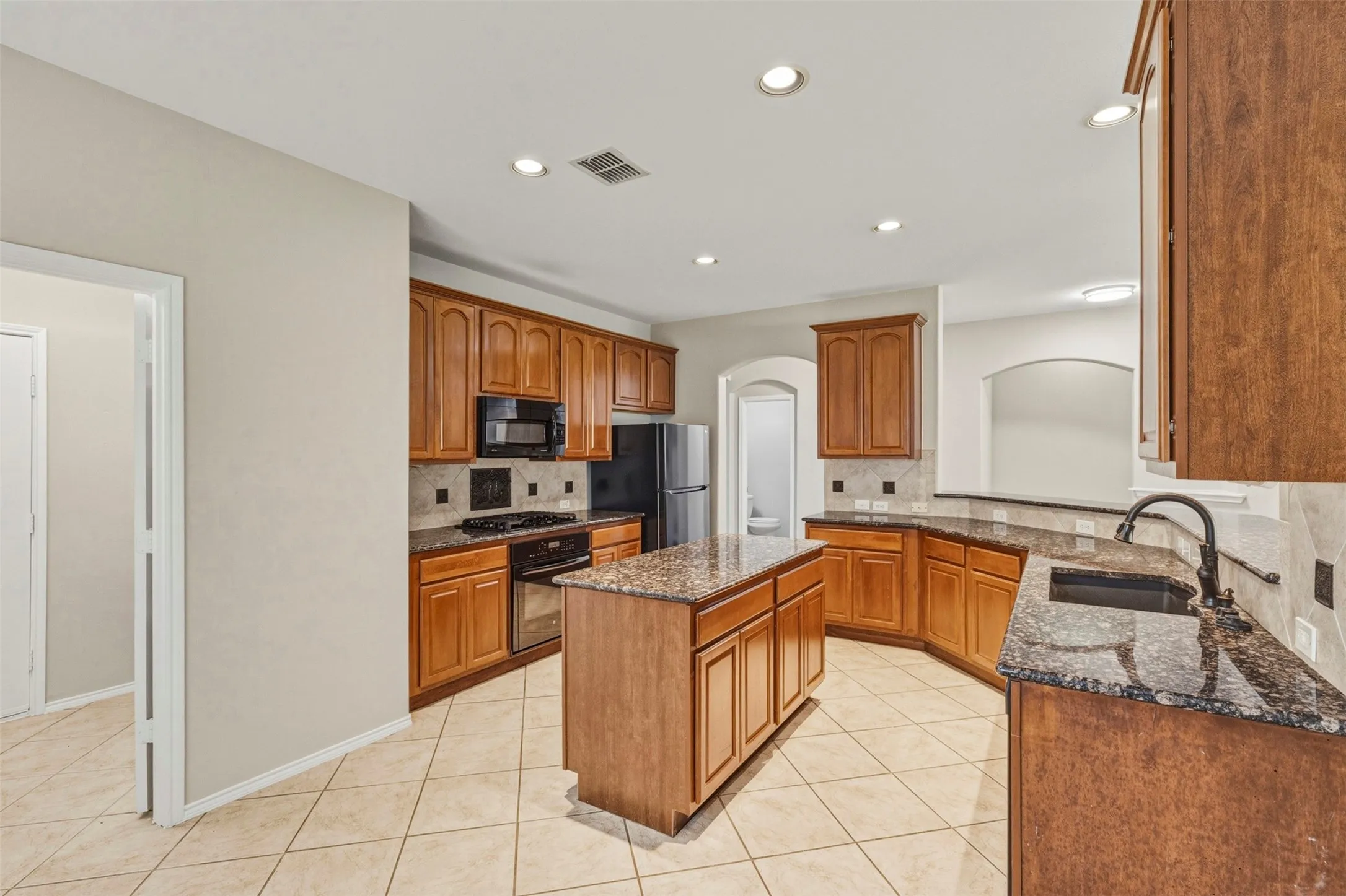 Kitchen featuring wood cabinetry, granite-finish countertops, tile flooring, and a central island