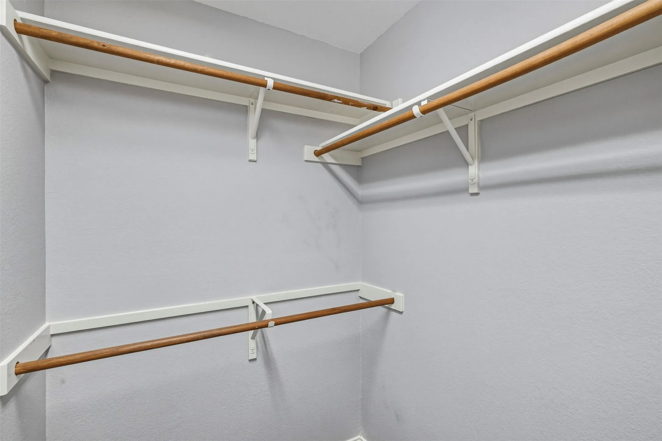 Walk-in closet with white shelving and wood-finish rods