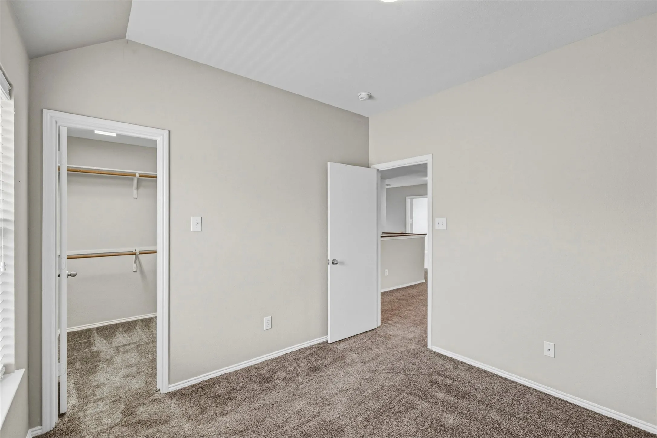 Vaulted ceiling, neutral tone walls, carpeted flooring, built-in closet shelving, and a white paneled door