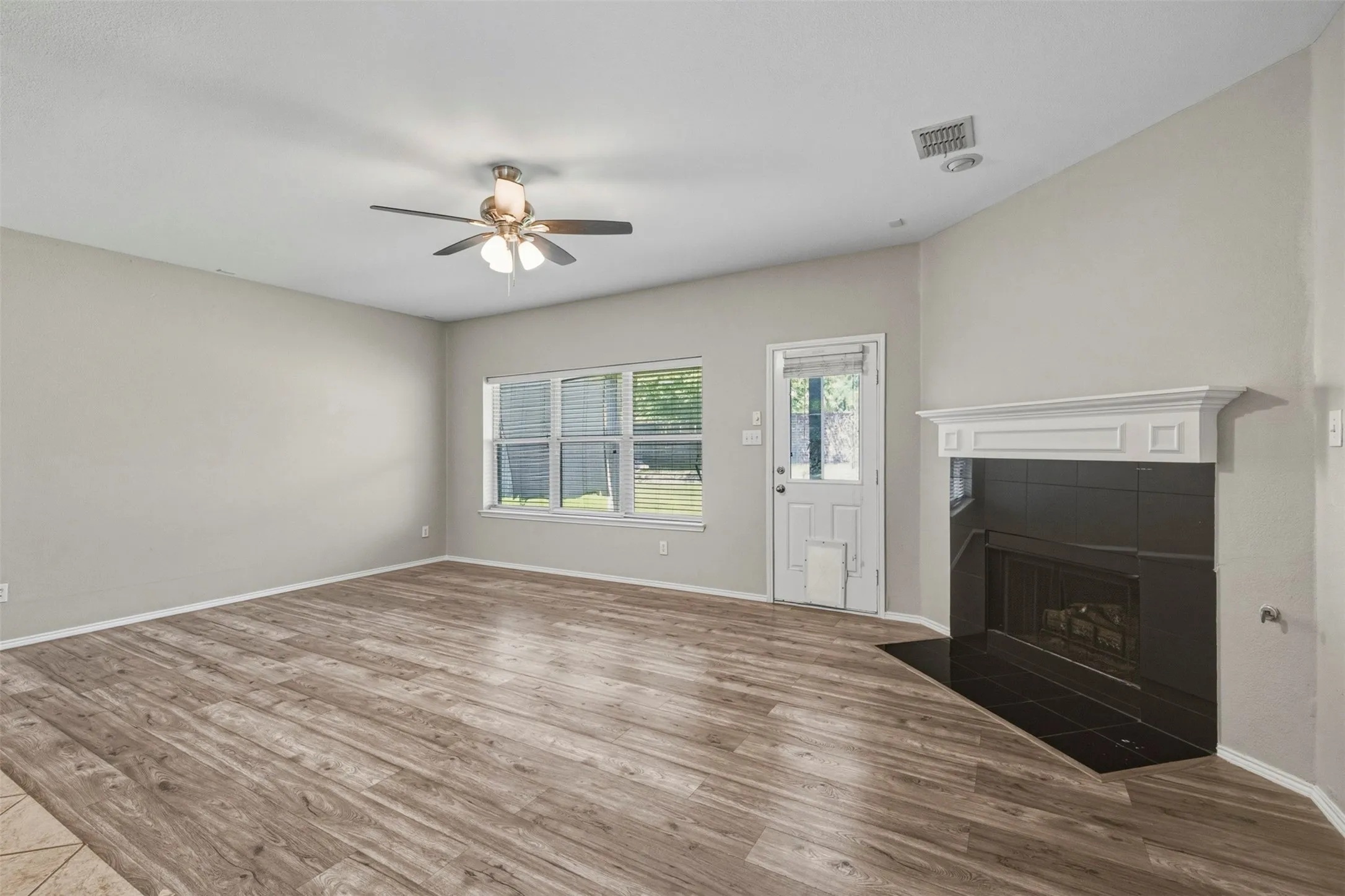 Spacious room featuring wood-finish flooring, a ceiling fan, and a corner fireplace with a black tile surround and white mantel