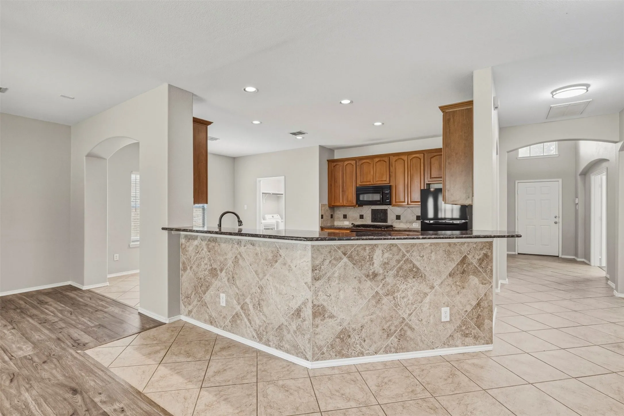 Kitchen island with stone tile facade and countertop, wood cabinetry, and recessed lighting
