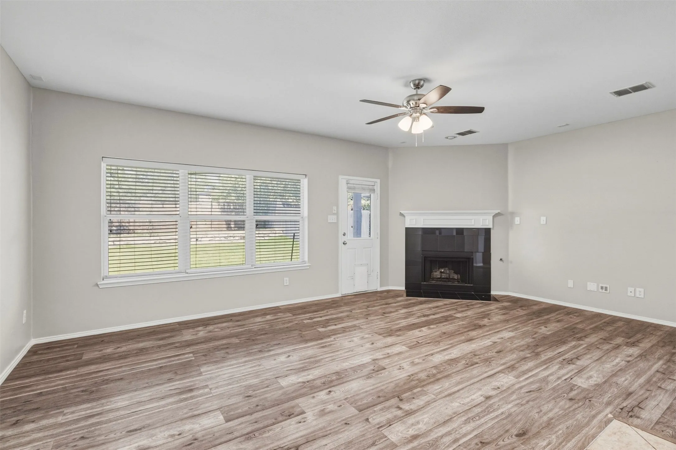 Wood-finish flooring, white walls, white trim, a ceiling fan with integrated lighting, and a fireplace with a white mantel and black surround