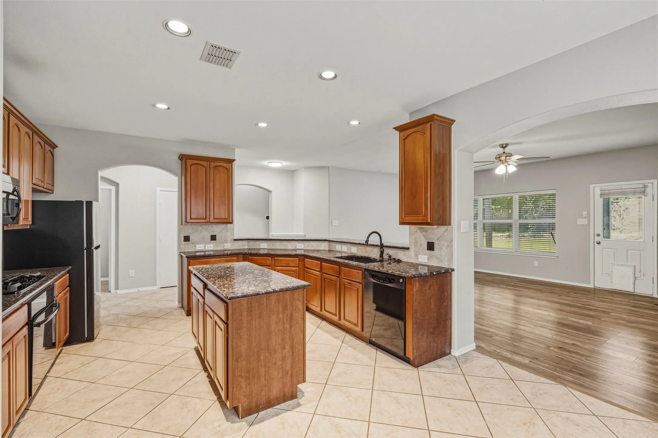 Kitchen featuring a central island, dark countertops, wood cabinetry, tile flooring, and recessed lighting