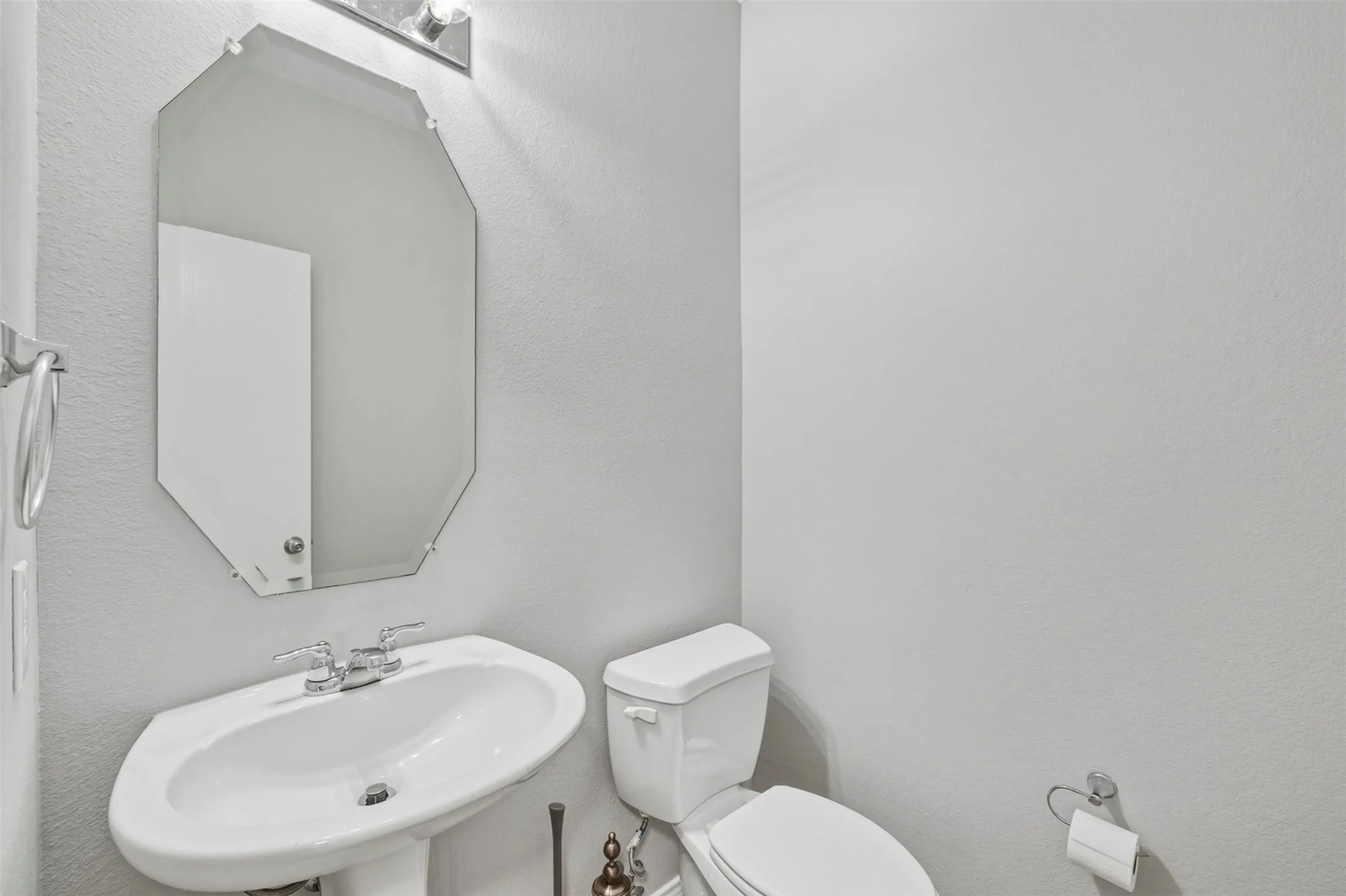 Pedestal sink, wall-mounted mirror, overhead vanity lighting, and toilet