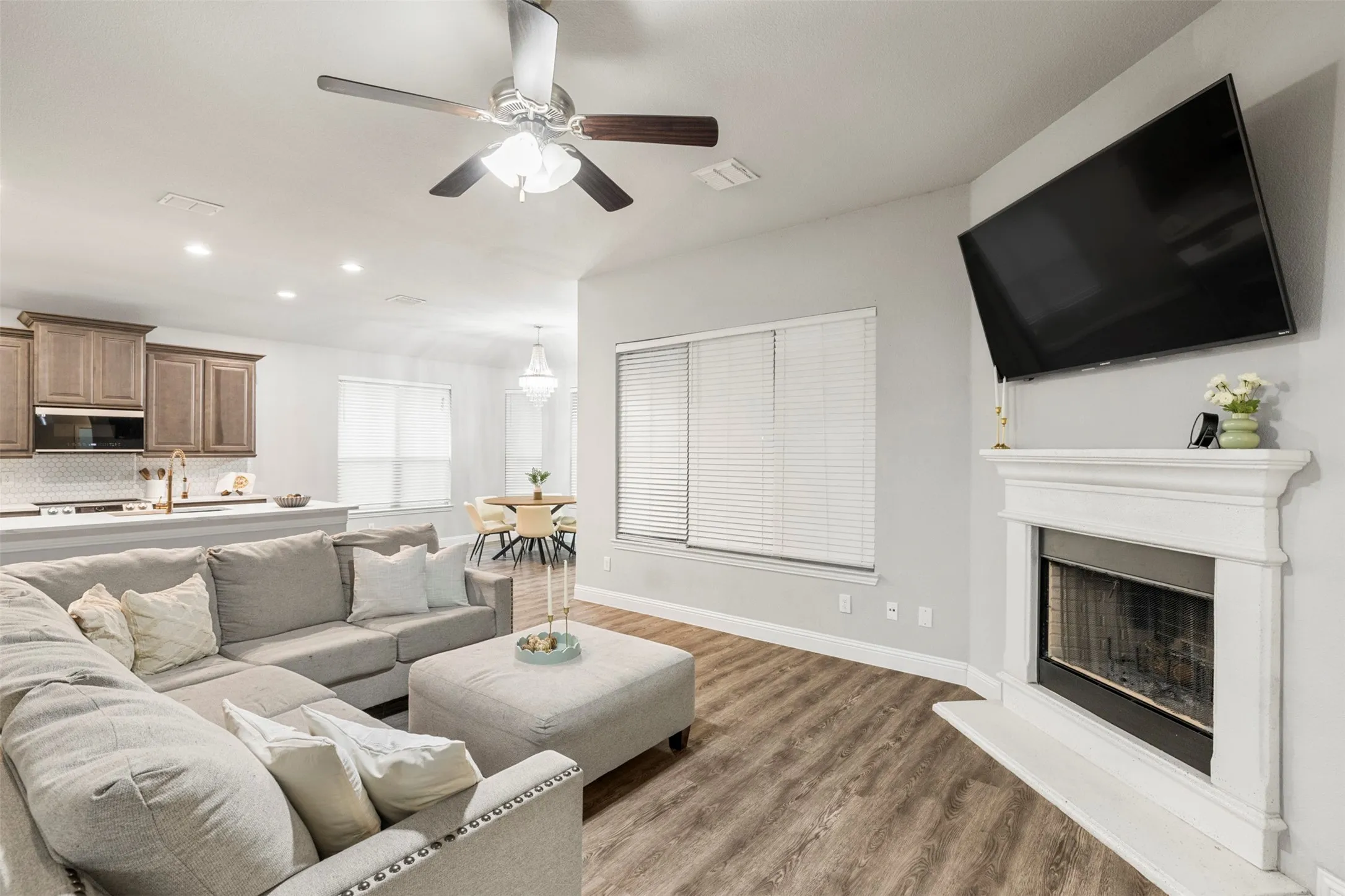 Living area featuring wood-finish flooring, a white mantel fireplace, and a ceiling fan