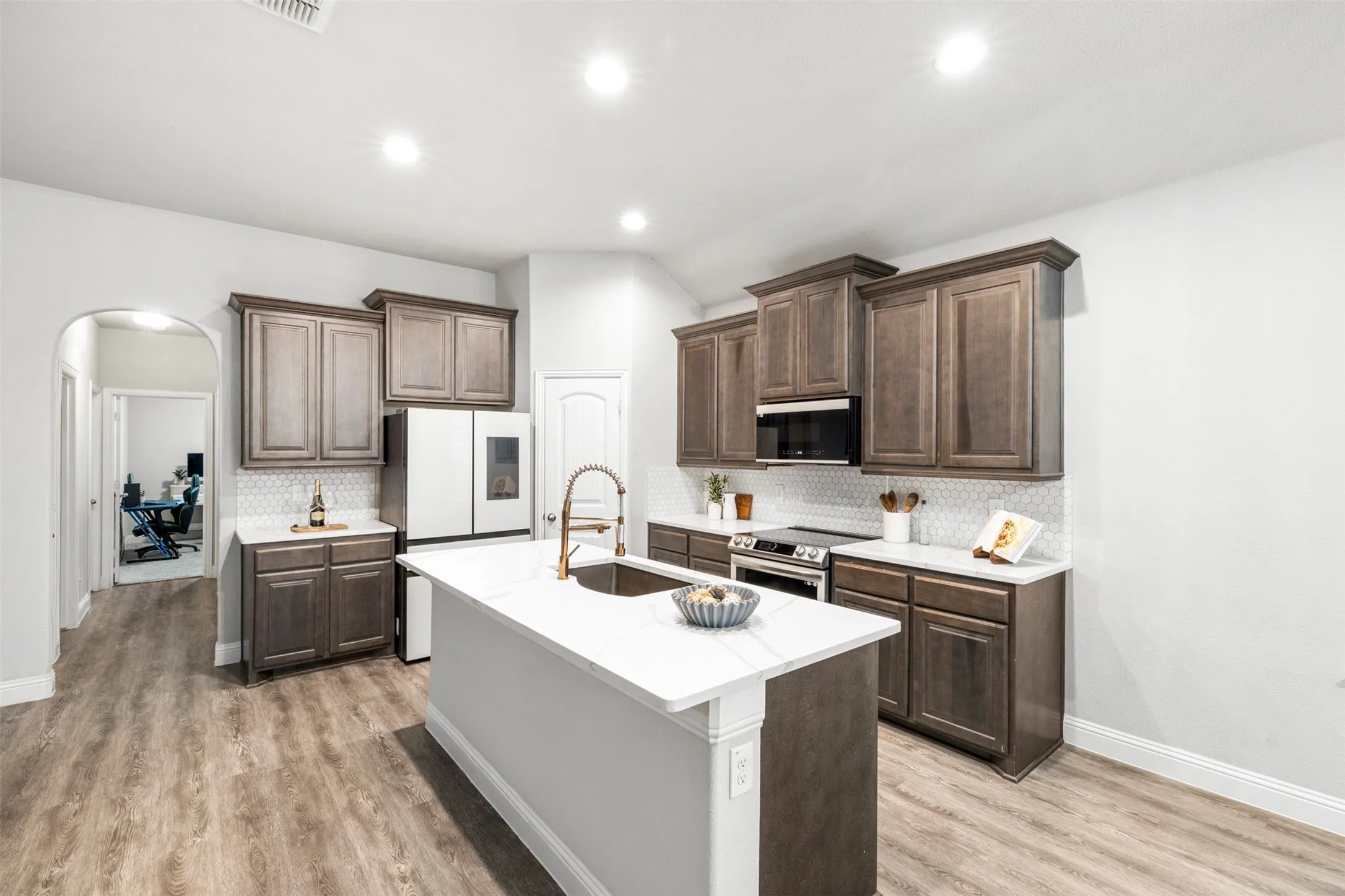 Kitchen featuring wood-finish flooring, shaker-style cabinetry, white countertops, and a central island with an integrated sink