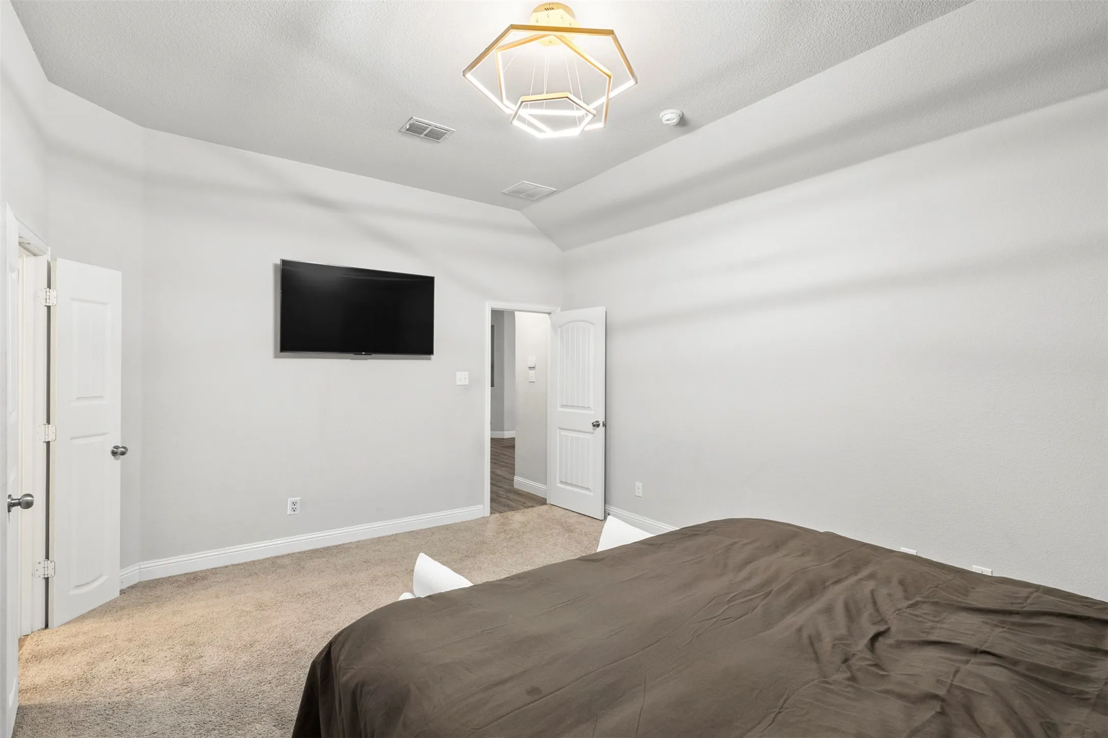 Vaulted ceiling with a geometric light fixture, light-toned carpeting, and white interior doors