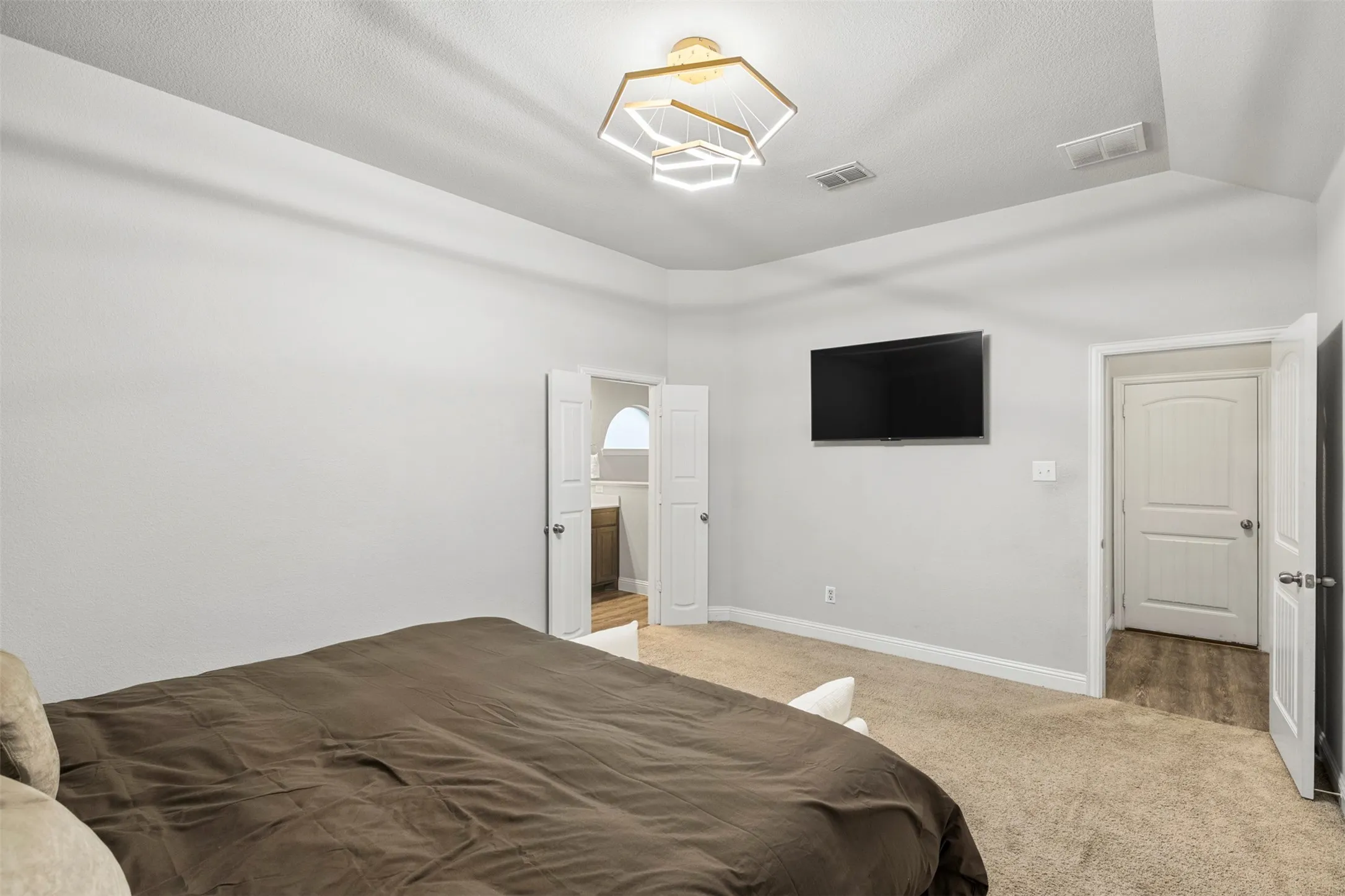 Vaulted ceiling with a geometric chandelier, neutral-toned carpeting, and light-colored walls