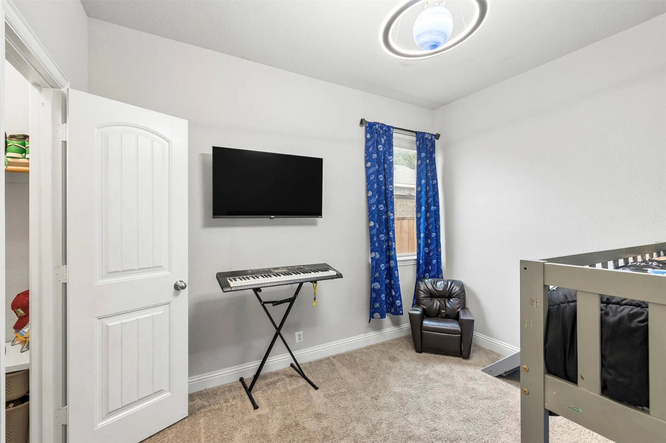 Carpeted room featuring a white paneled door, a mounted television, a window with curtains, and a contemporary ceiling light fixture