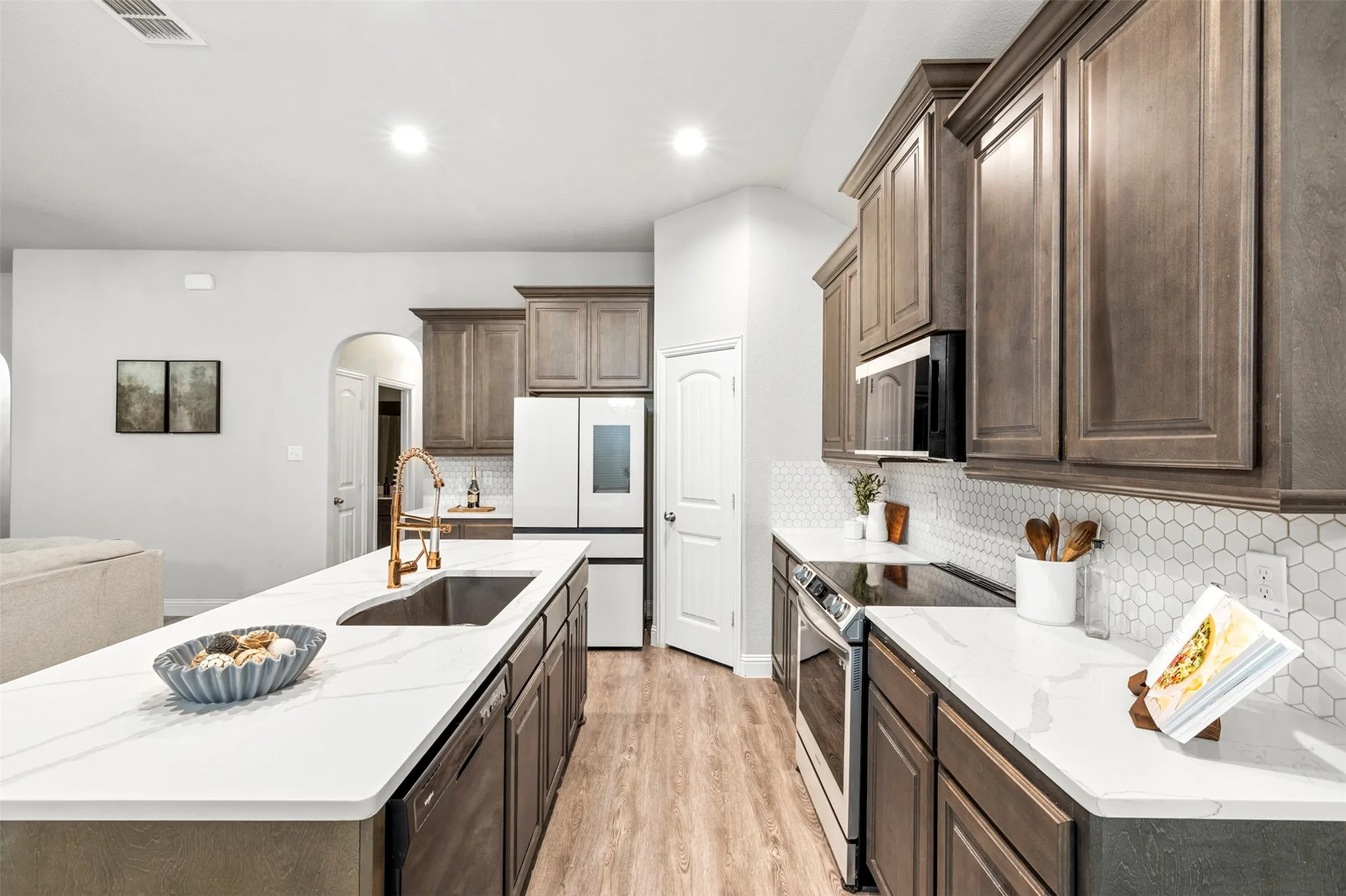 Spacious kitchen featuring an expansive island, white quartz countertops, full-height hex tile backsplash, and wood-finish cabinetry
