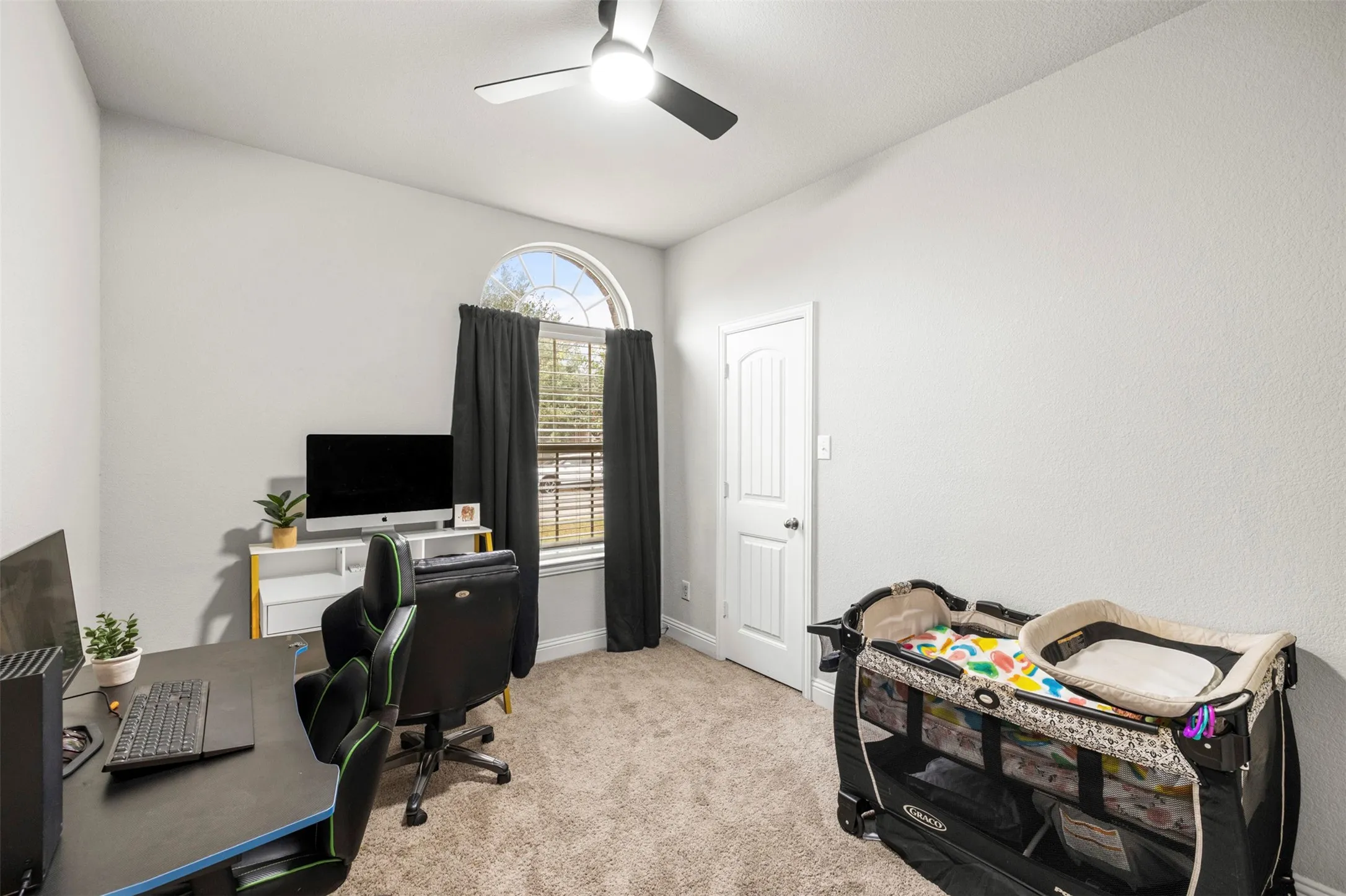 Arched window, ceiling fan, textured walls, carpet flooring, and a paneled door