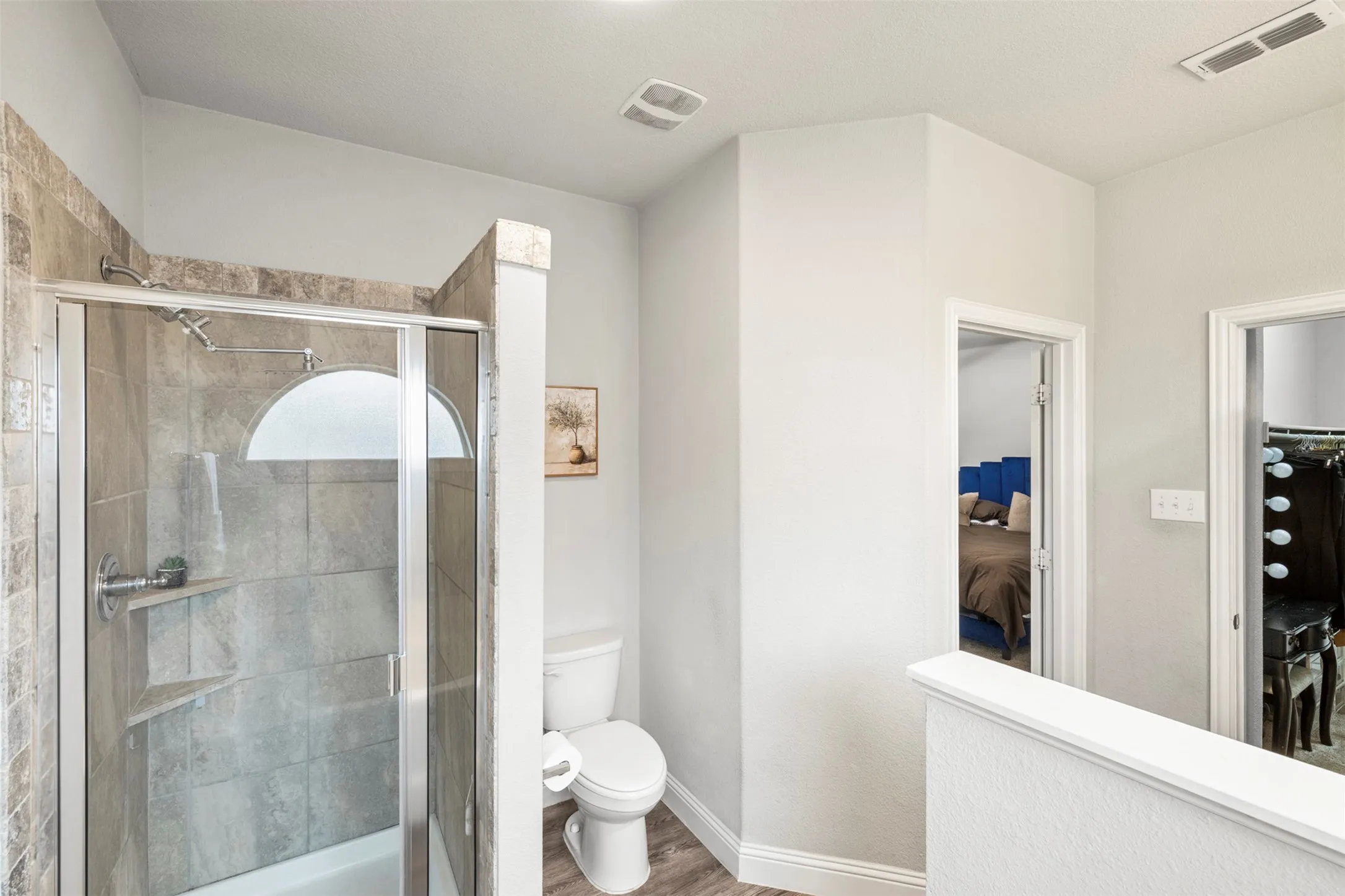 Tiled shower enclosure with a glass door, built-in shelving, and a toilet with wood-finish flooring
