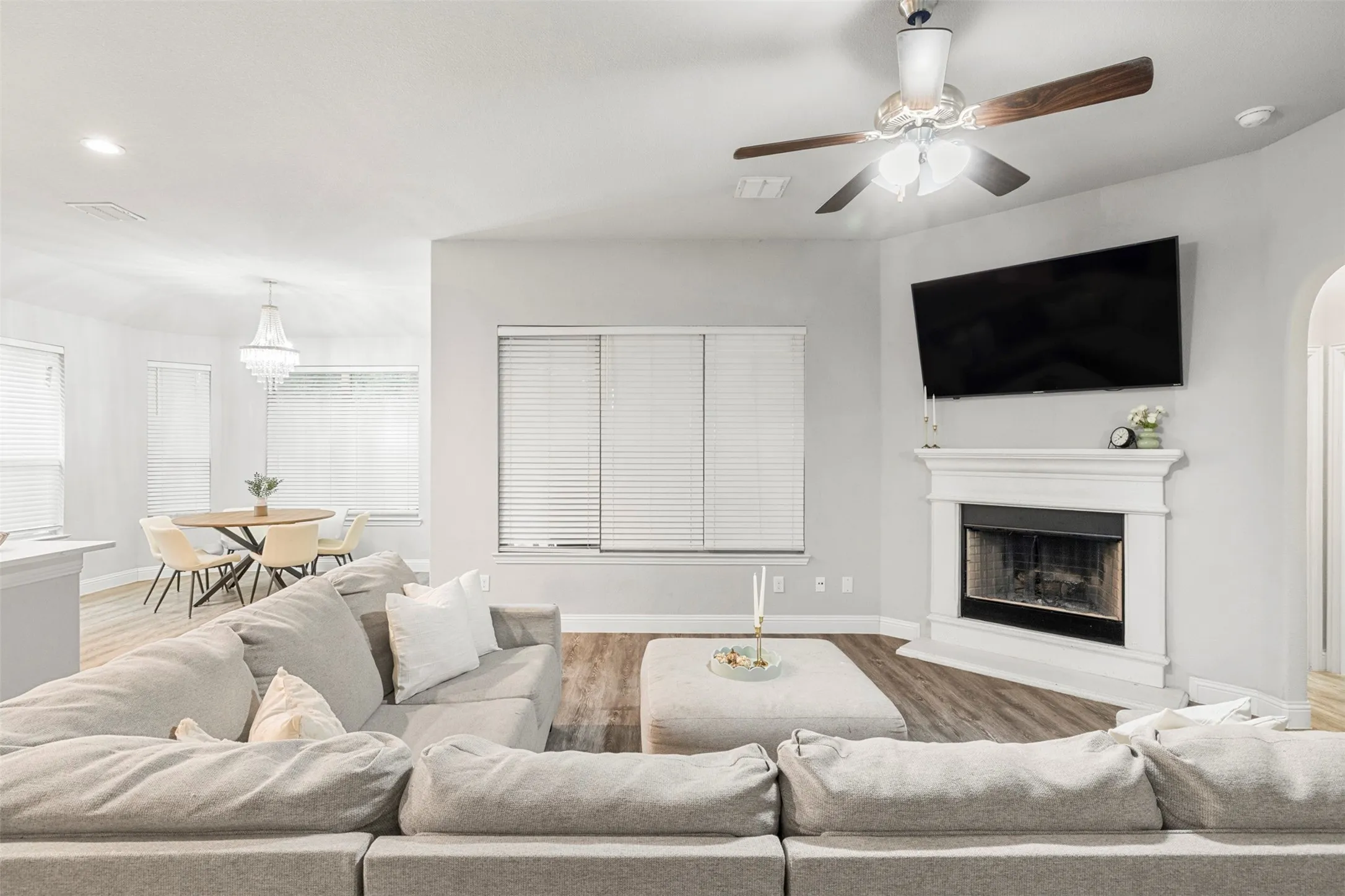 Hardwood-finish flooring, white mantel fireplace, ceiling fan with wood-finish blades, recessed lighting, and an arched doorway