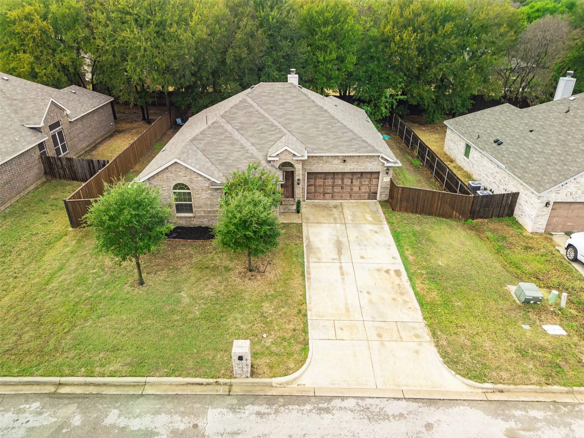 Stone facade residence featuring an attached garage with wood-finish doors, a concrete driveway, and a shingled roof