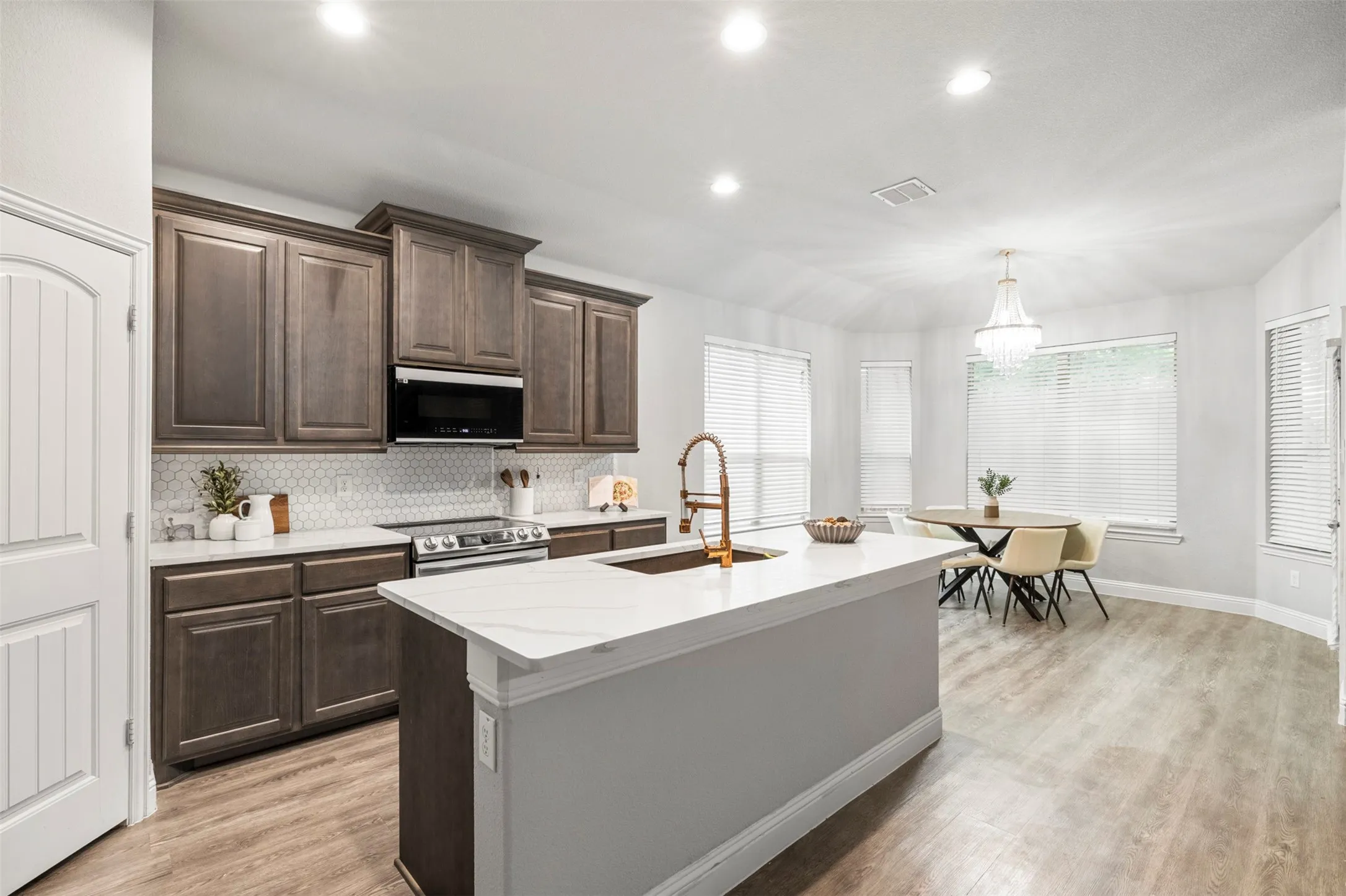 Kitchen featuring wood-finish cabinetry, white hexagonal tile backsplash, stainless steel range, and a kitchen island with a white countertop and integrated sink