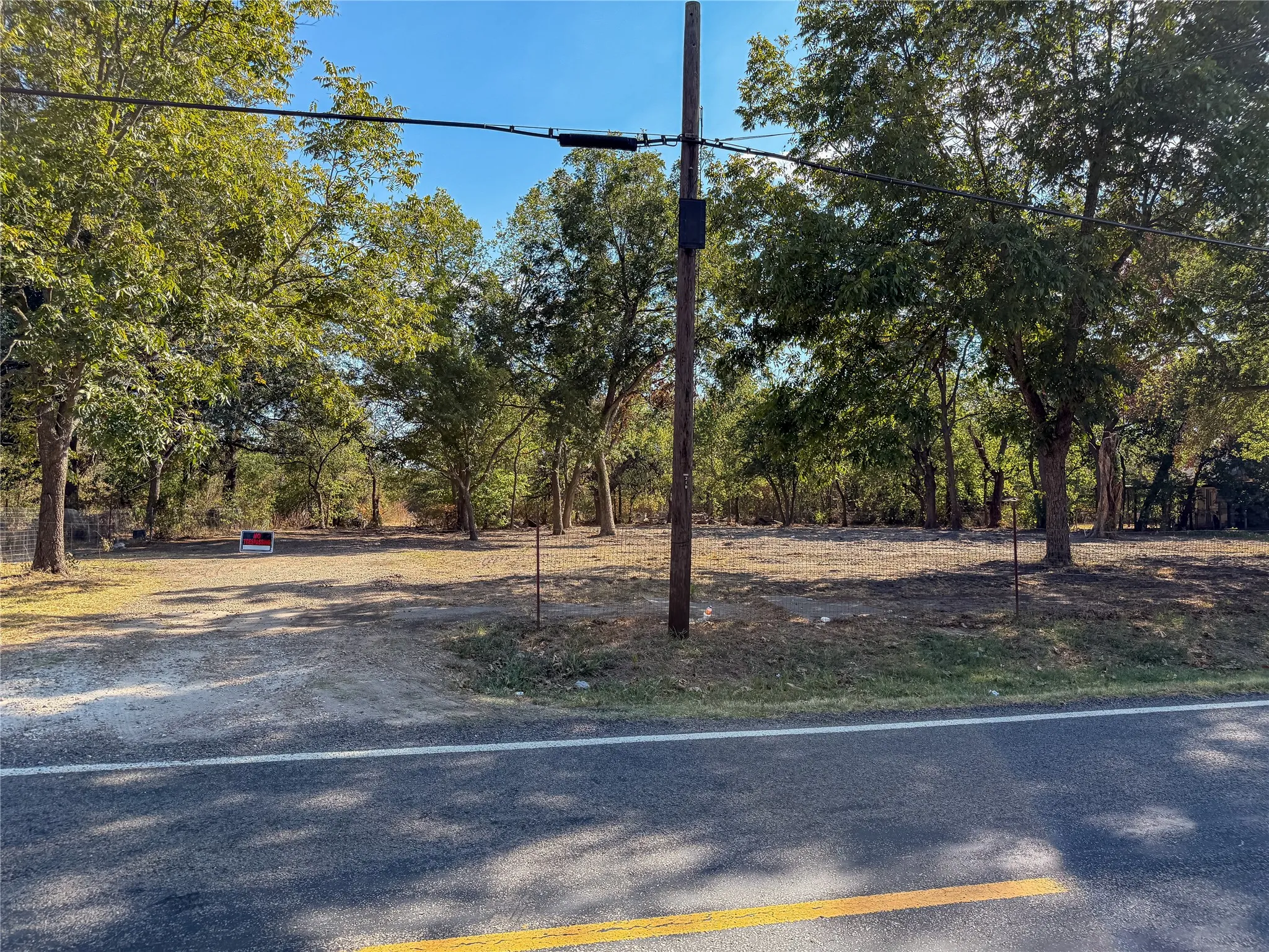 Roadside property featuring a cleared building site, mature trees, and natural landscaping