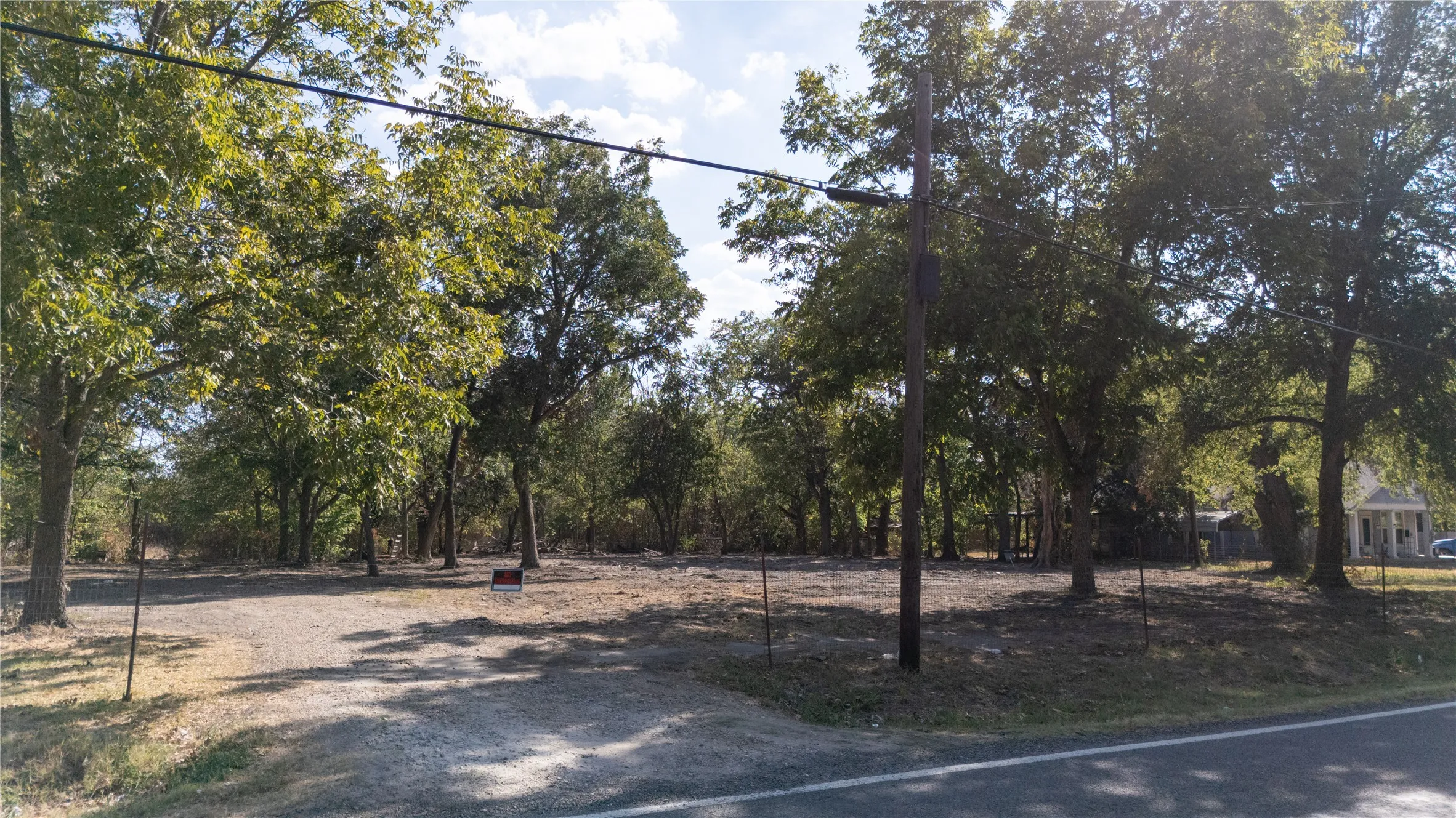Gravel lot with mature trees and a paved road frontage