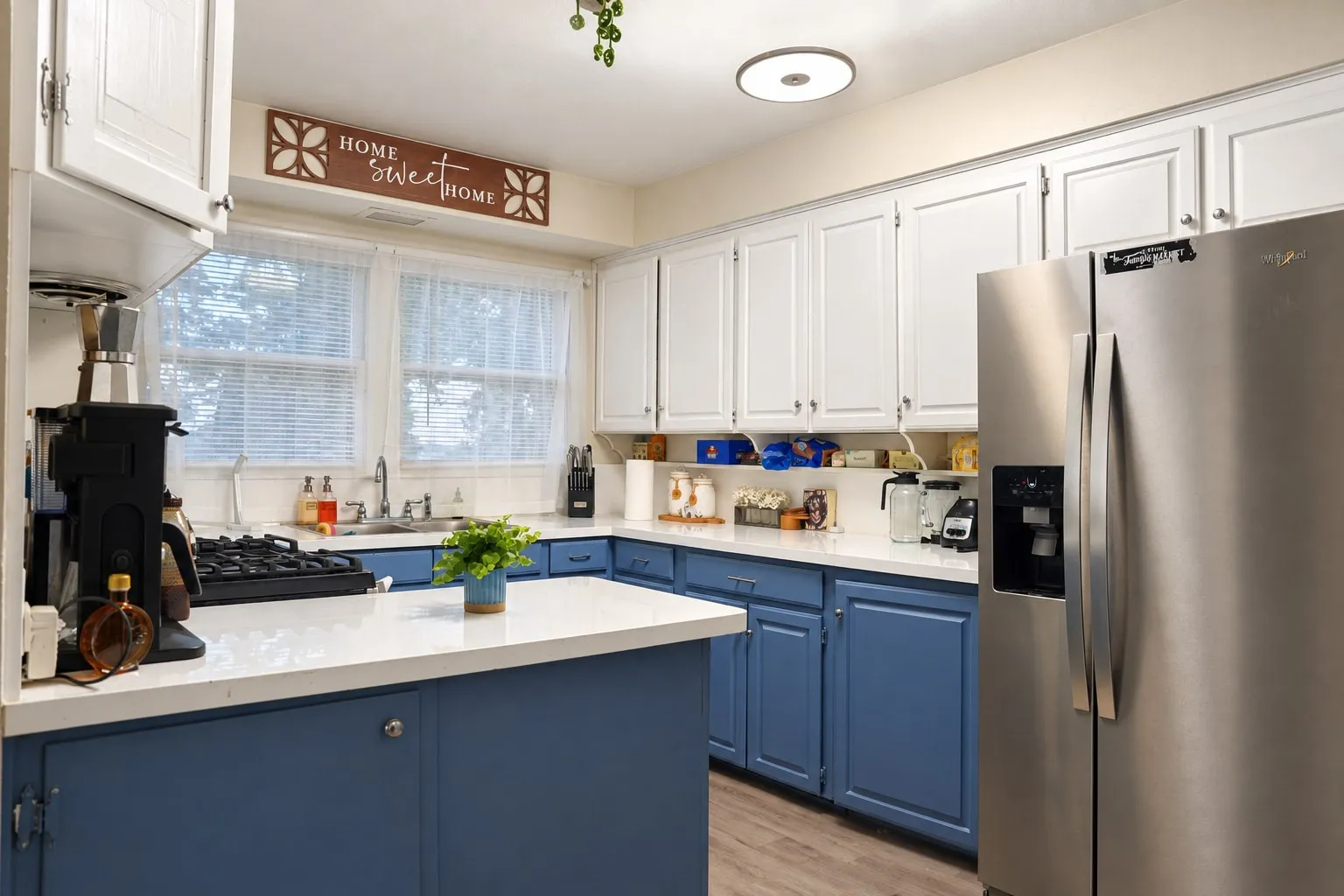Two-toned cabinetry with white upper and blue lower cabinets, light-toned countertops, wood-finish flooring, and a stainless steel side-by-side refrigerator