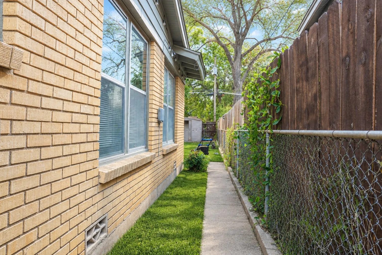 Brick exterior with multiple windows, concrete walkway, and a wooden privacy fence