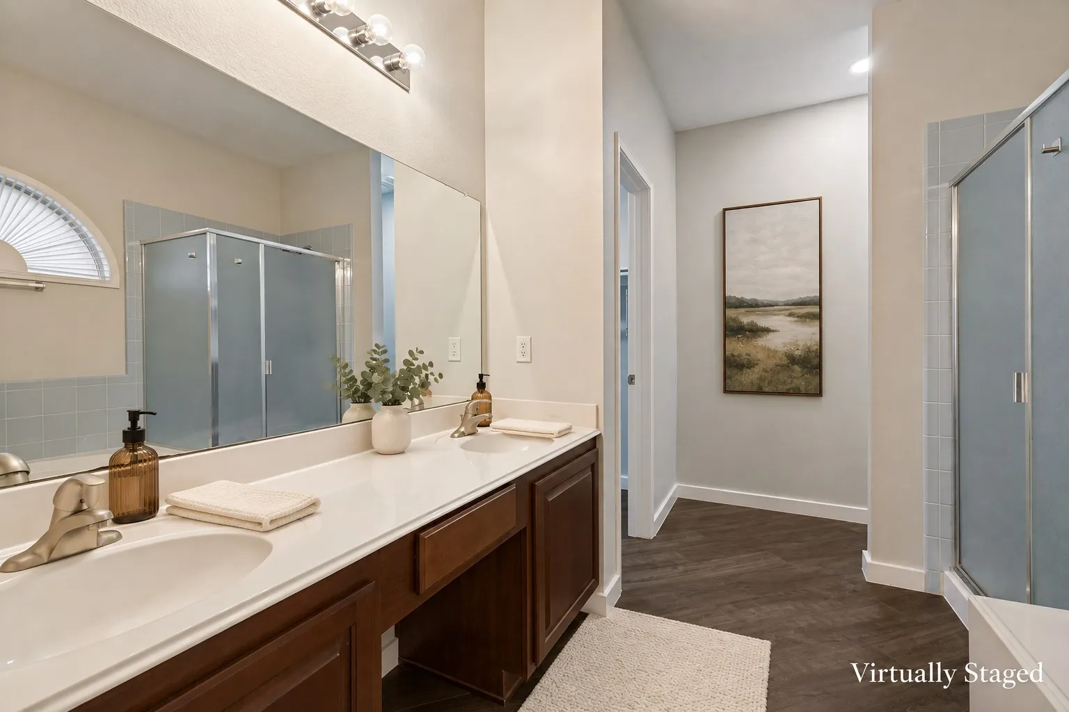 Primary bathroom featuring a built-in tub, a frosted glass shower enclosure, a double vanity with an integrated countertop, and wood-finish flooring expansive mirror, and a three-light fixture