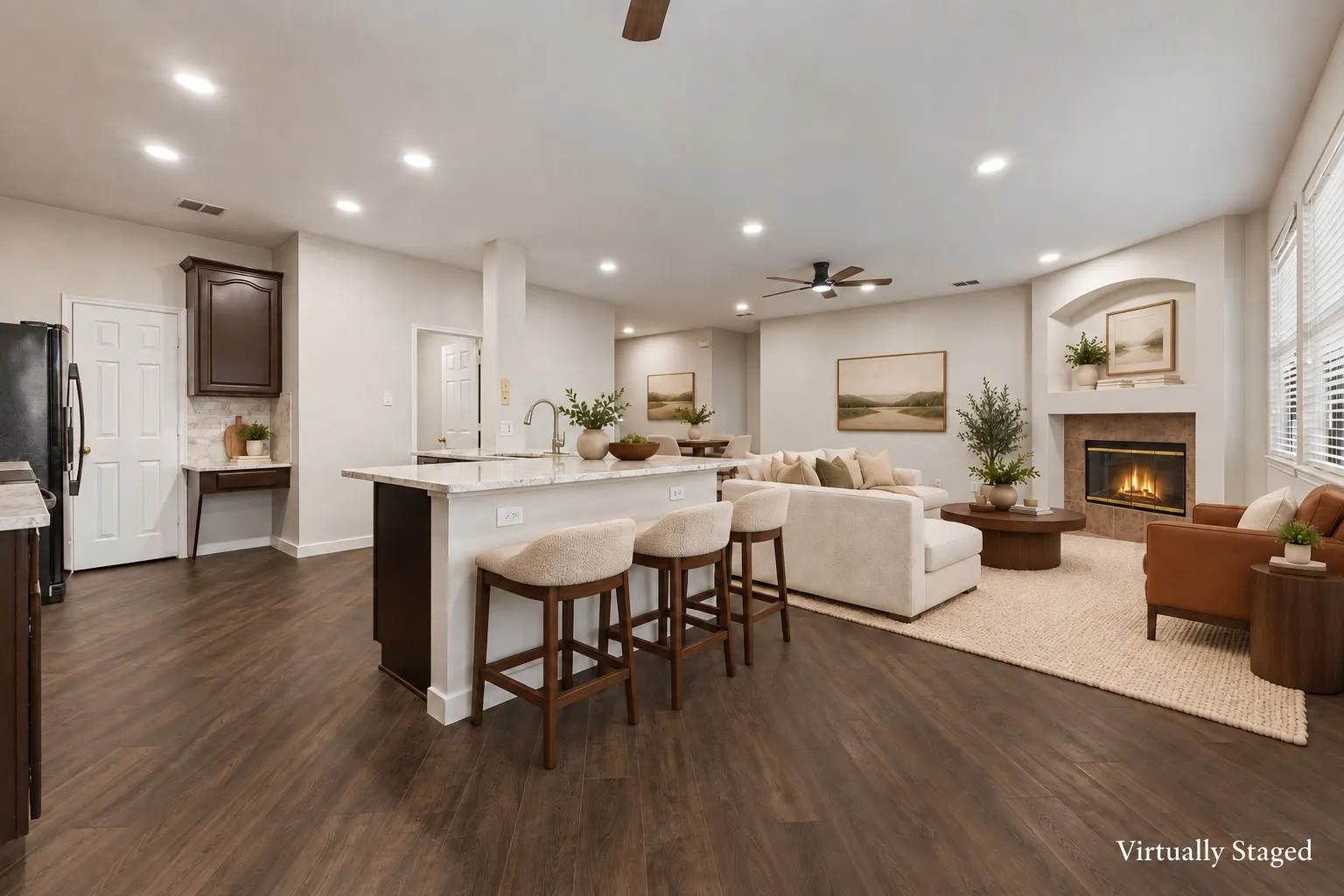 Open-concept living area featuring wood-finish flooring, a kitchen island with seating, a built-in fireplace, and recessed lighting.