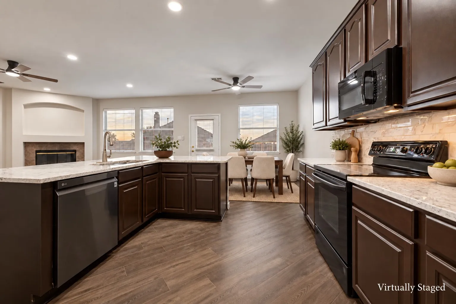 Open-concept kitchen featuring wood-finish flooring, dark wood cabinetry, light-toned countertops, and stainless steel appliances