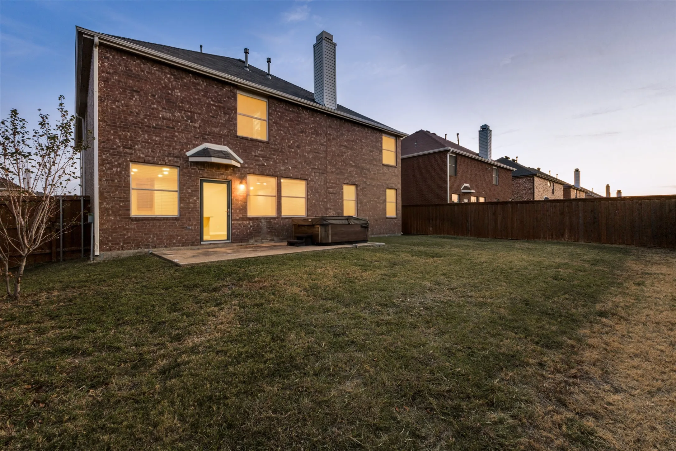 Brick exterior with multiple windows, concrete patio, and a privacy fence enclosing a grassy yard