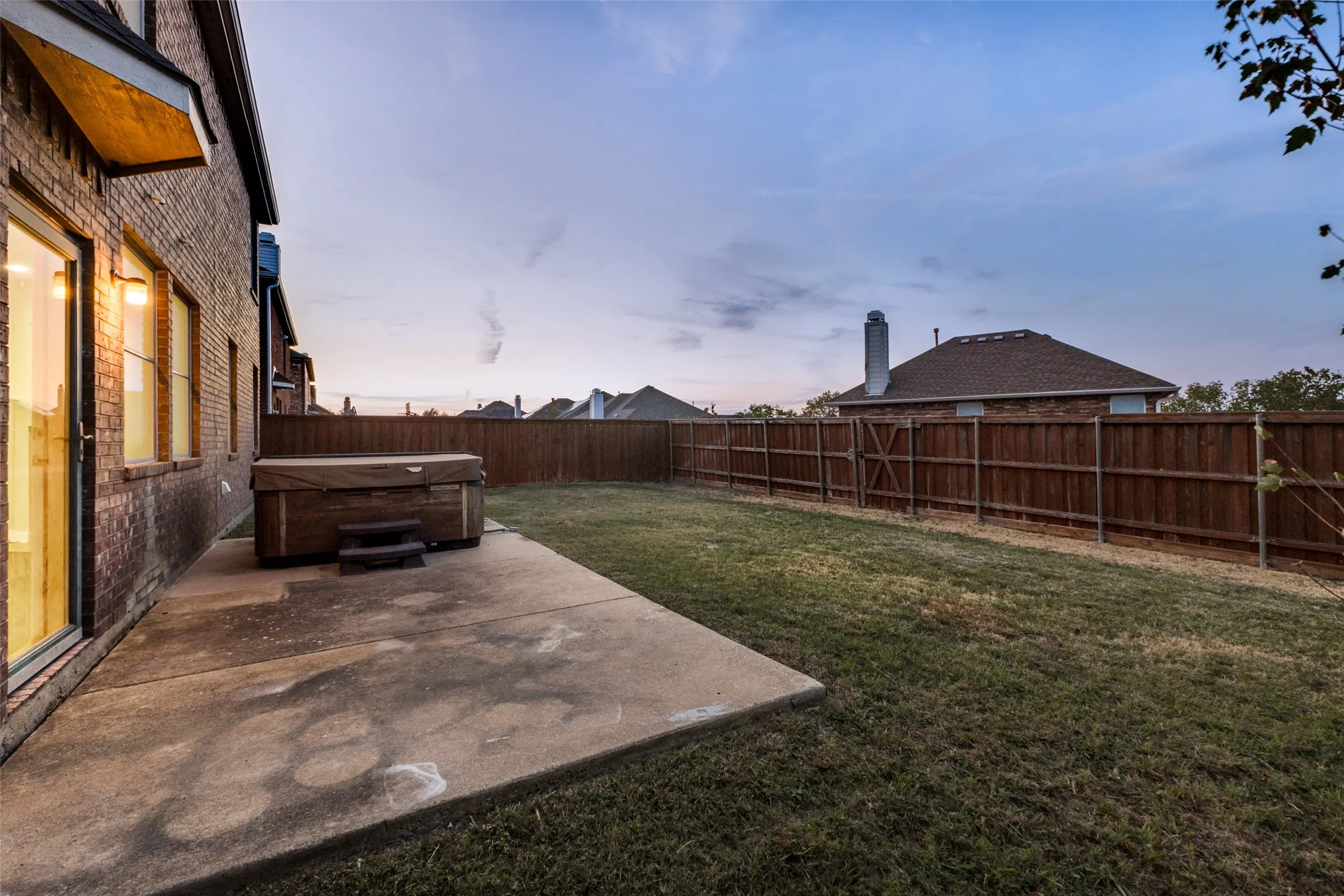 Expansive backyard featuring a privacy fence, concrete patio, and hot tub