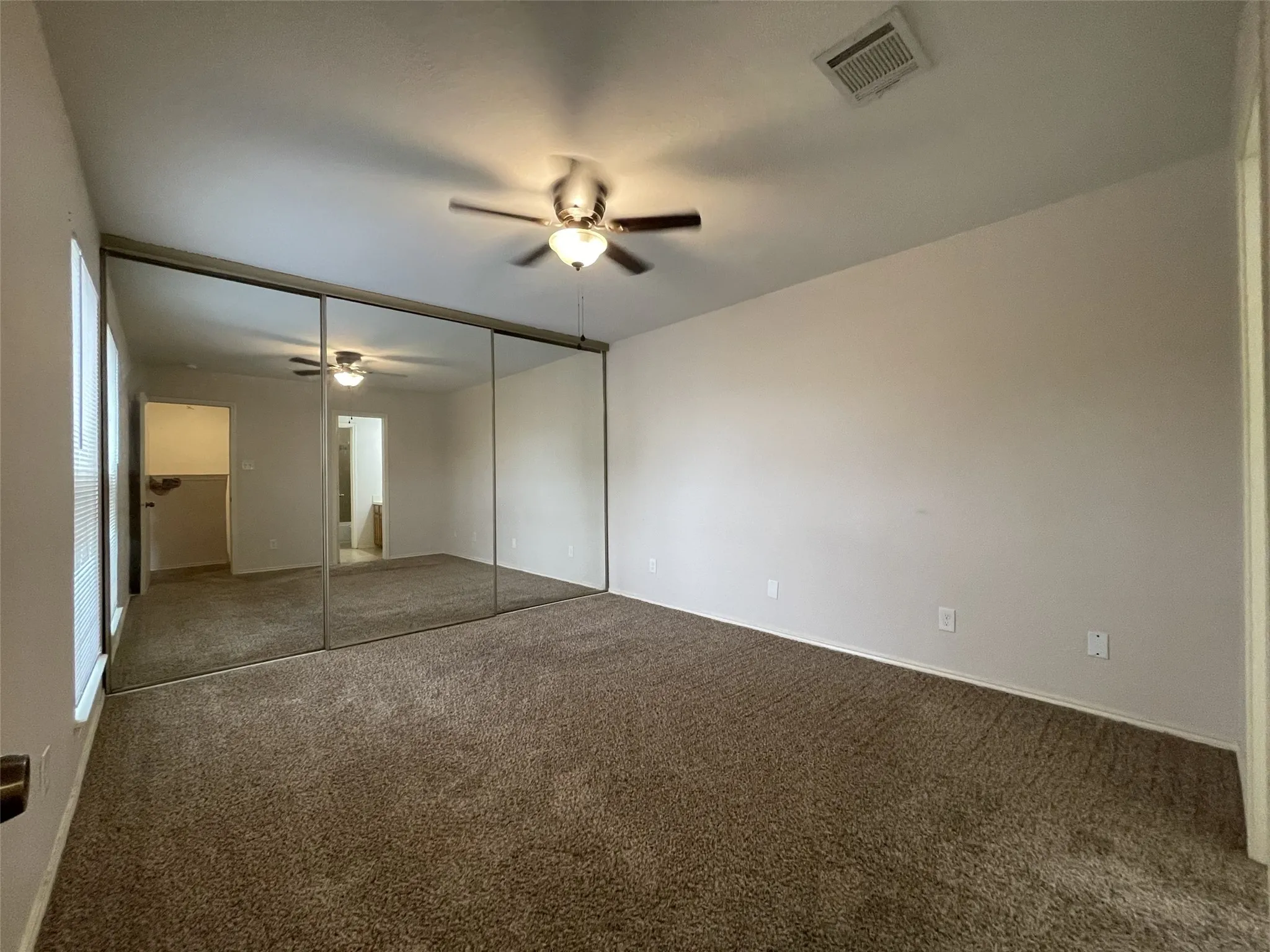 Wall-to-wall mirrored closet doors, neutral tone carpet, ceiling fan with integrated lighting, and white painted walls
