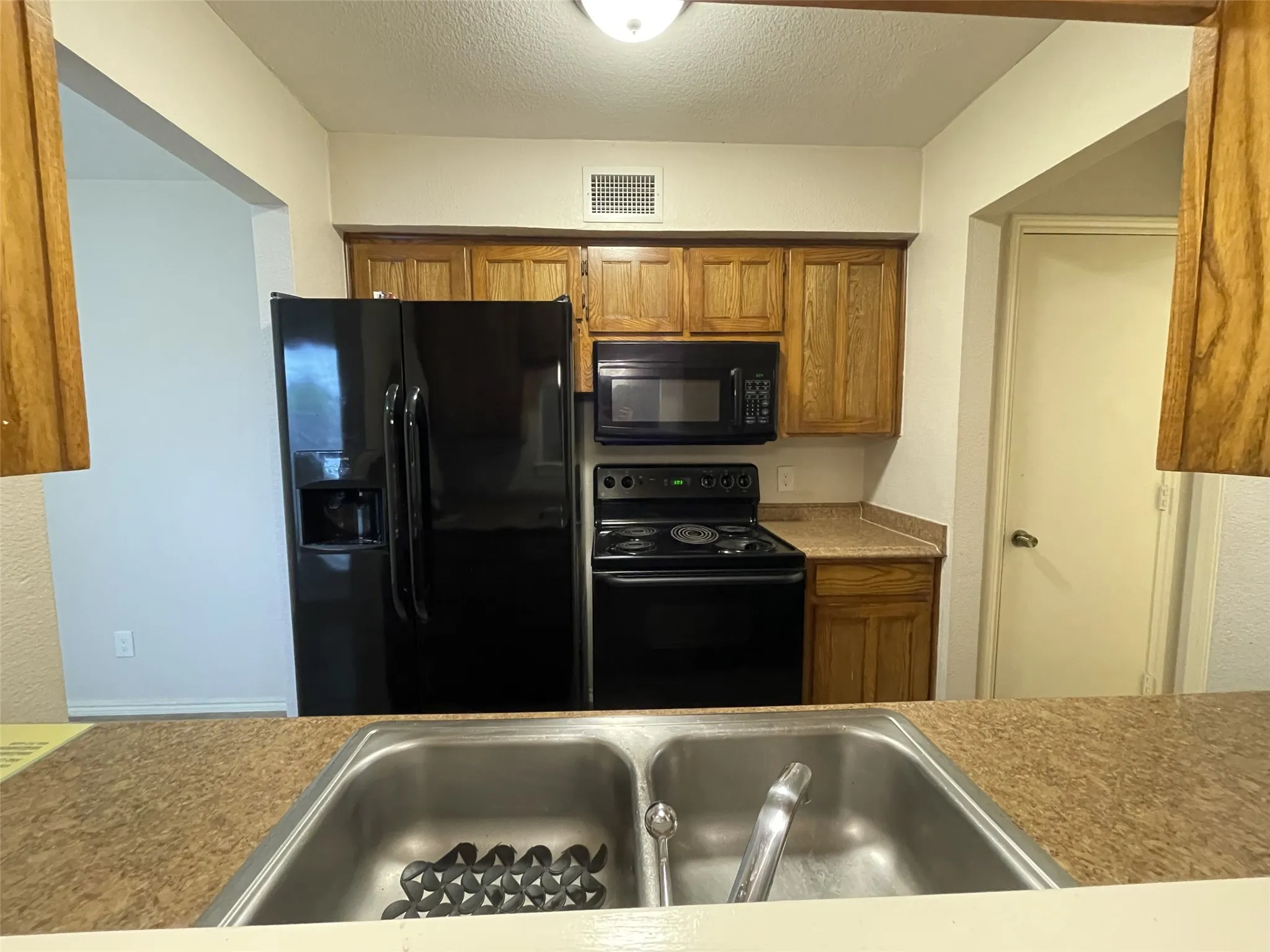 Kitchen featuring wood cabinetry, black appliances, a double basin stainless steel sink, and speckled countertops